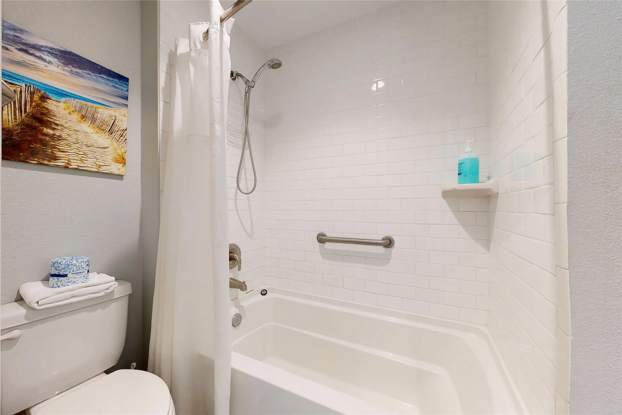 Bathtub and shower combination with subway tile surround, brushed nickel fixtures, and a wall-mounted grab bar