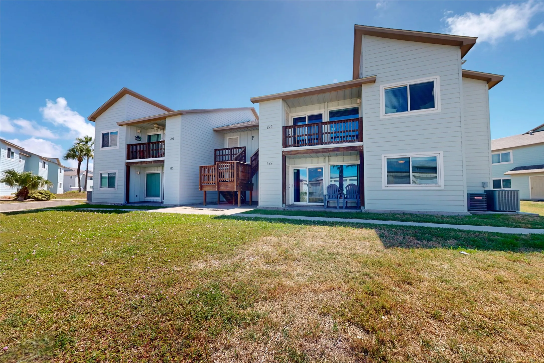 Building featuring light blue siding, white trim windows, and two balconies with wood railings