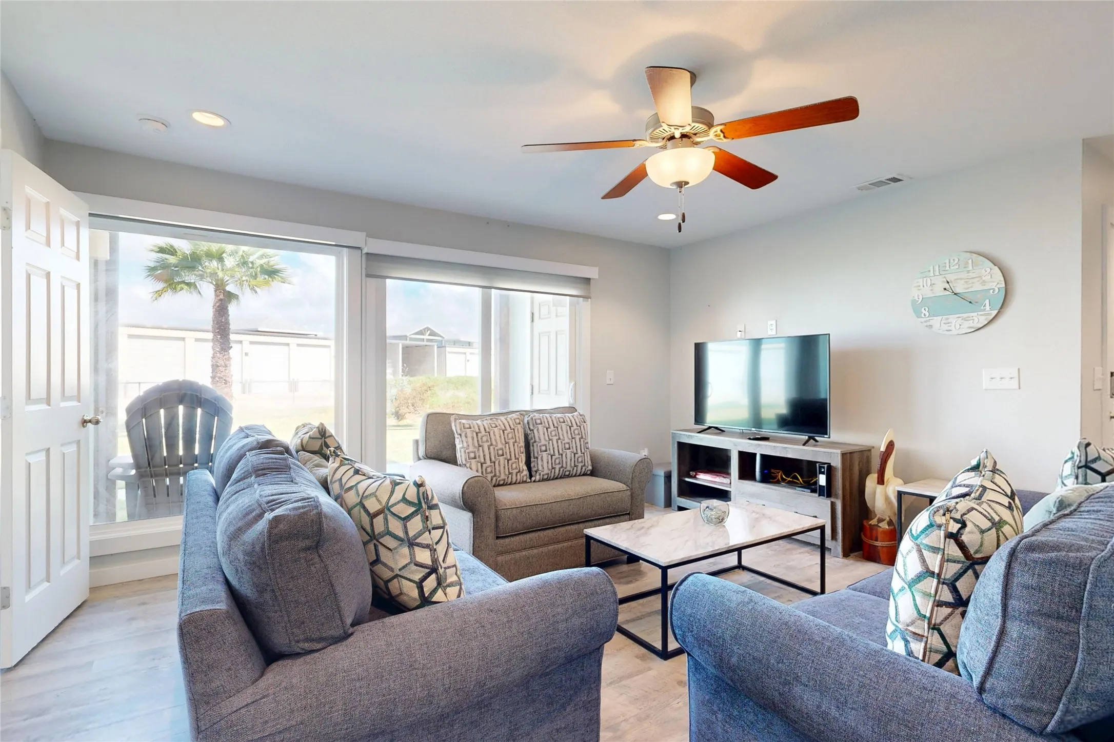 Recessed ceiling lighting, a ceiling fan with light fixture, wood-finish flooring, and large windows