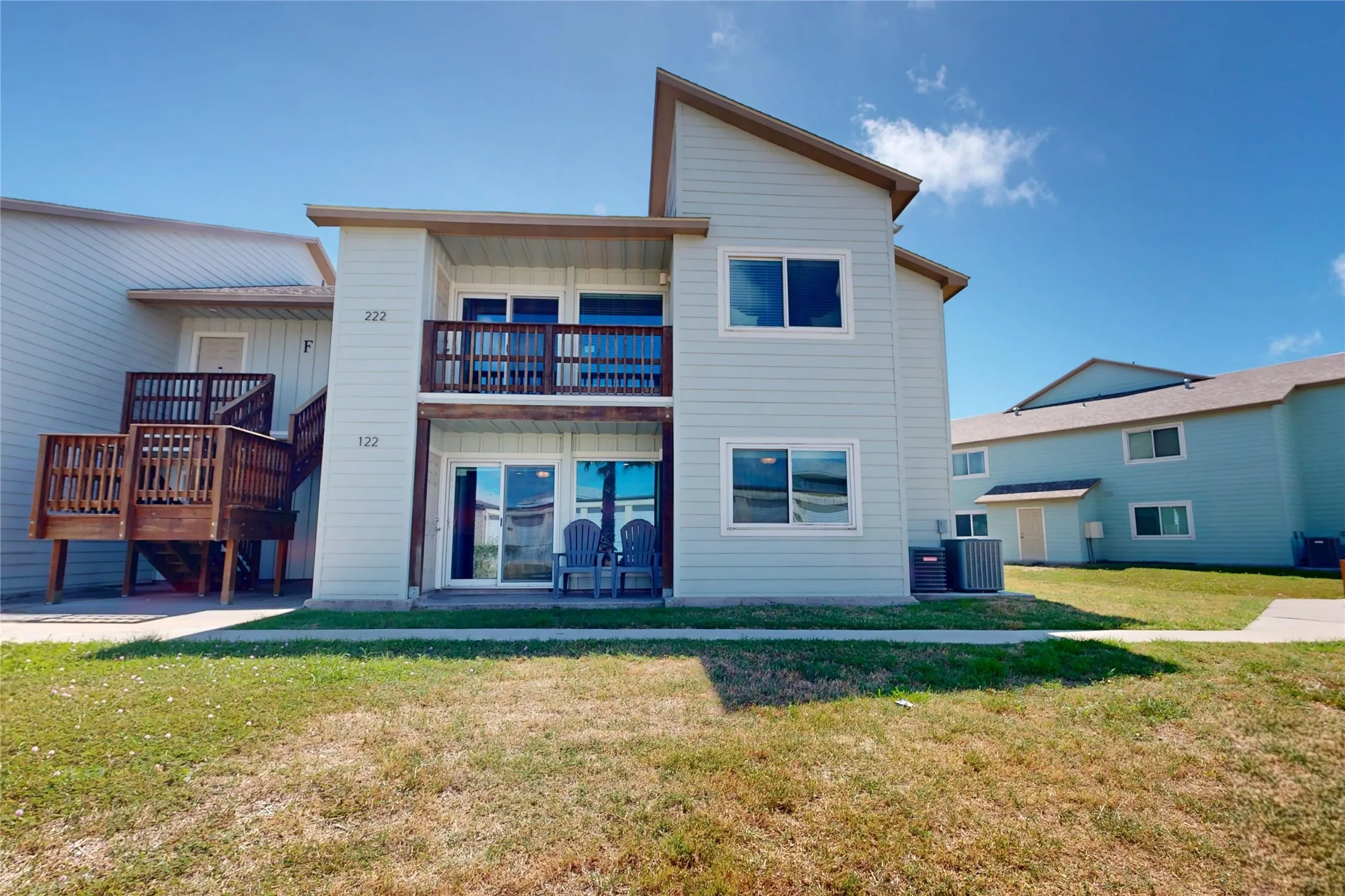 1st floor condo residence featuring light blue siding, an upper-level balcony with wood railing, and a ground-level patio