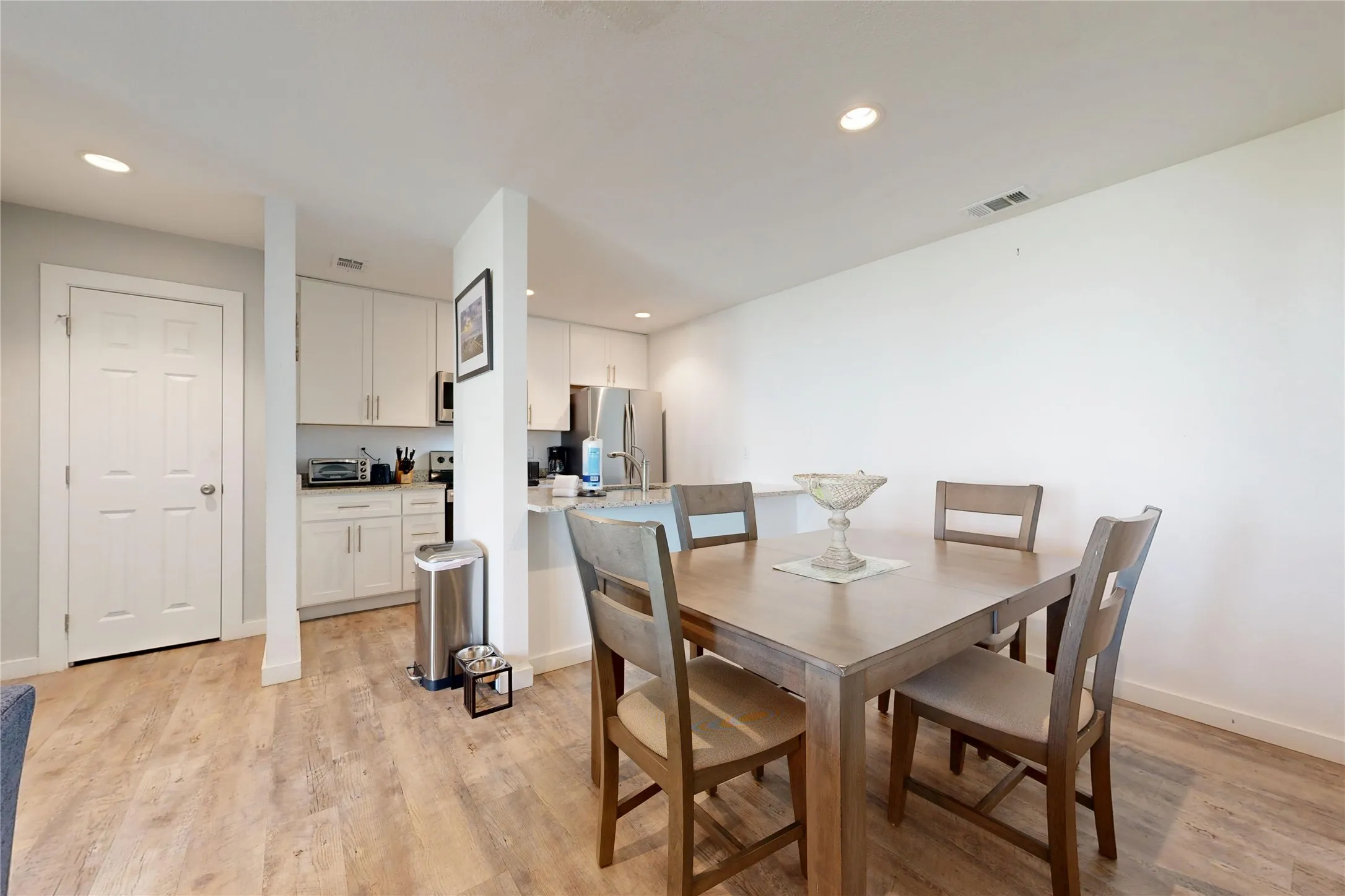 Open-concept living space with wood-finish flooring, recessed lighting, and a kitchen featuring white cabinetry and stainless steel appliances