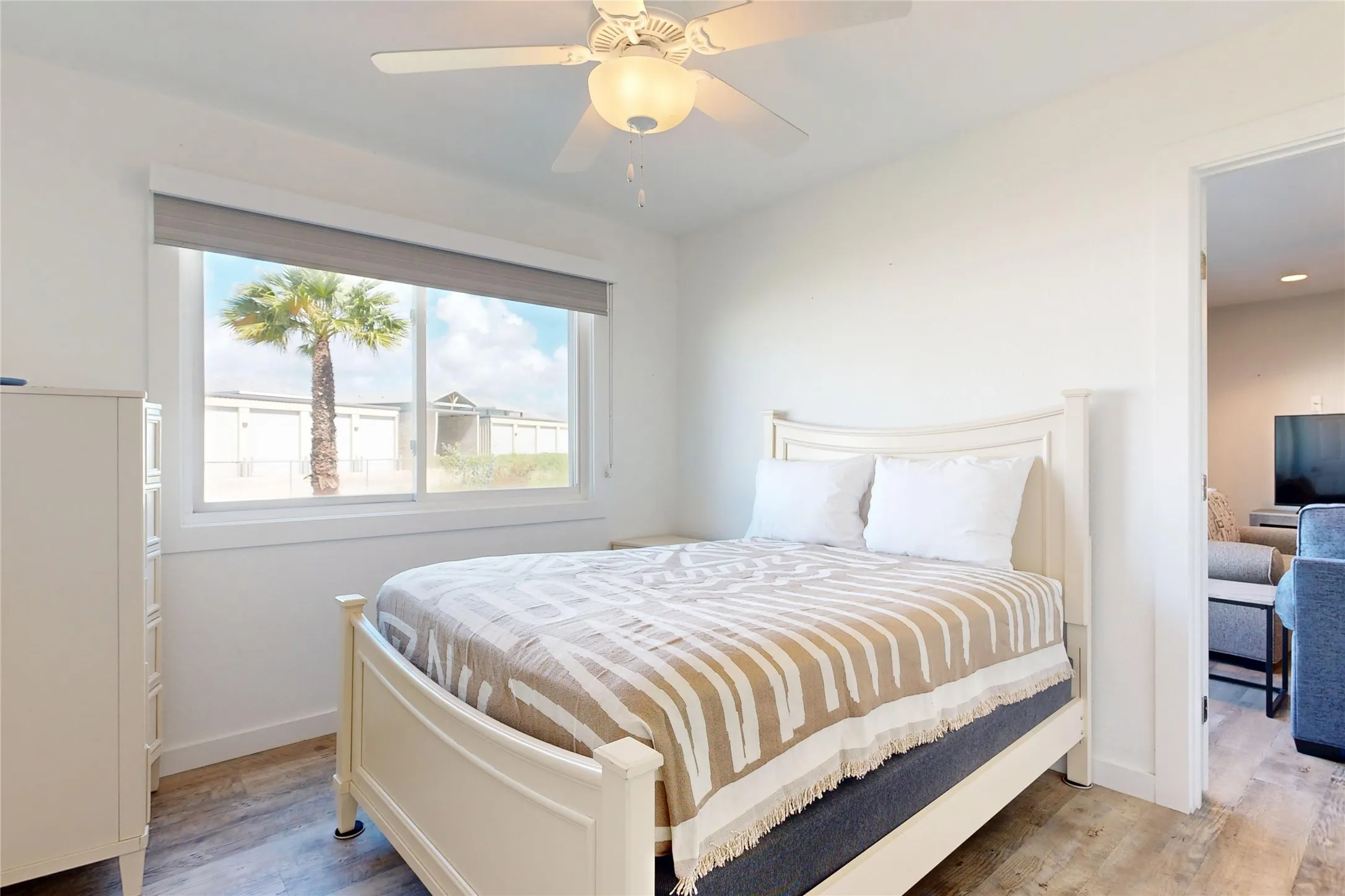 White ceiling fan with integrated lighting, window with roller shade, wood-finish flooring, and white trim
