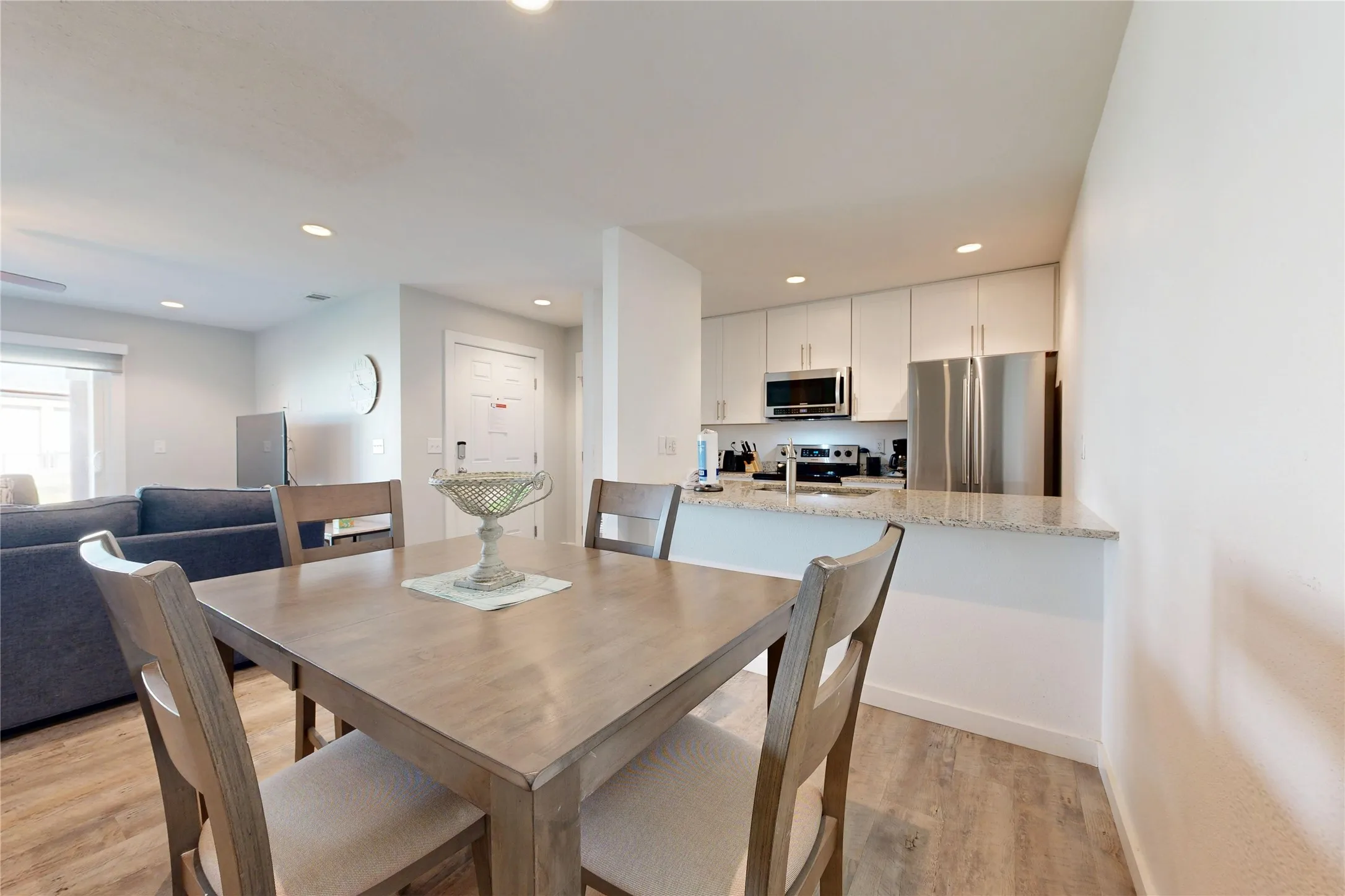 Open-concept living area featuring wood-finish flooring, recessed lighting, and a kitchen with white cabinetry, stainless steel appliances, and a light-toned countertop