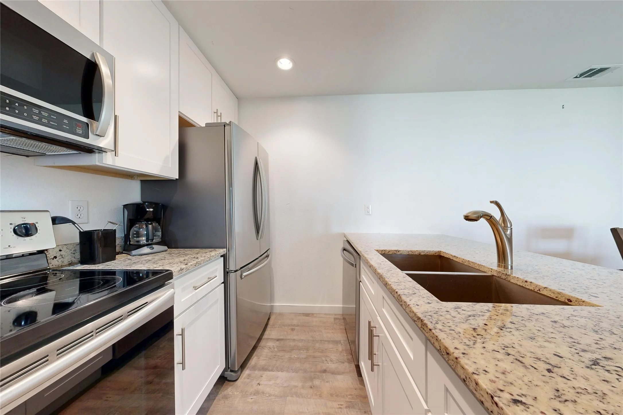 Kitchen featuring stainless steel appliances, white cabinetry, wood-finish flooring, recessed lighting, and a double basin sink with a gooseneck faucet