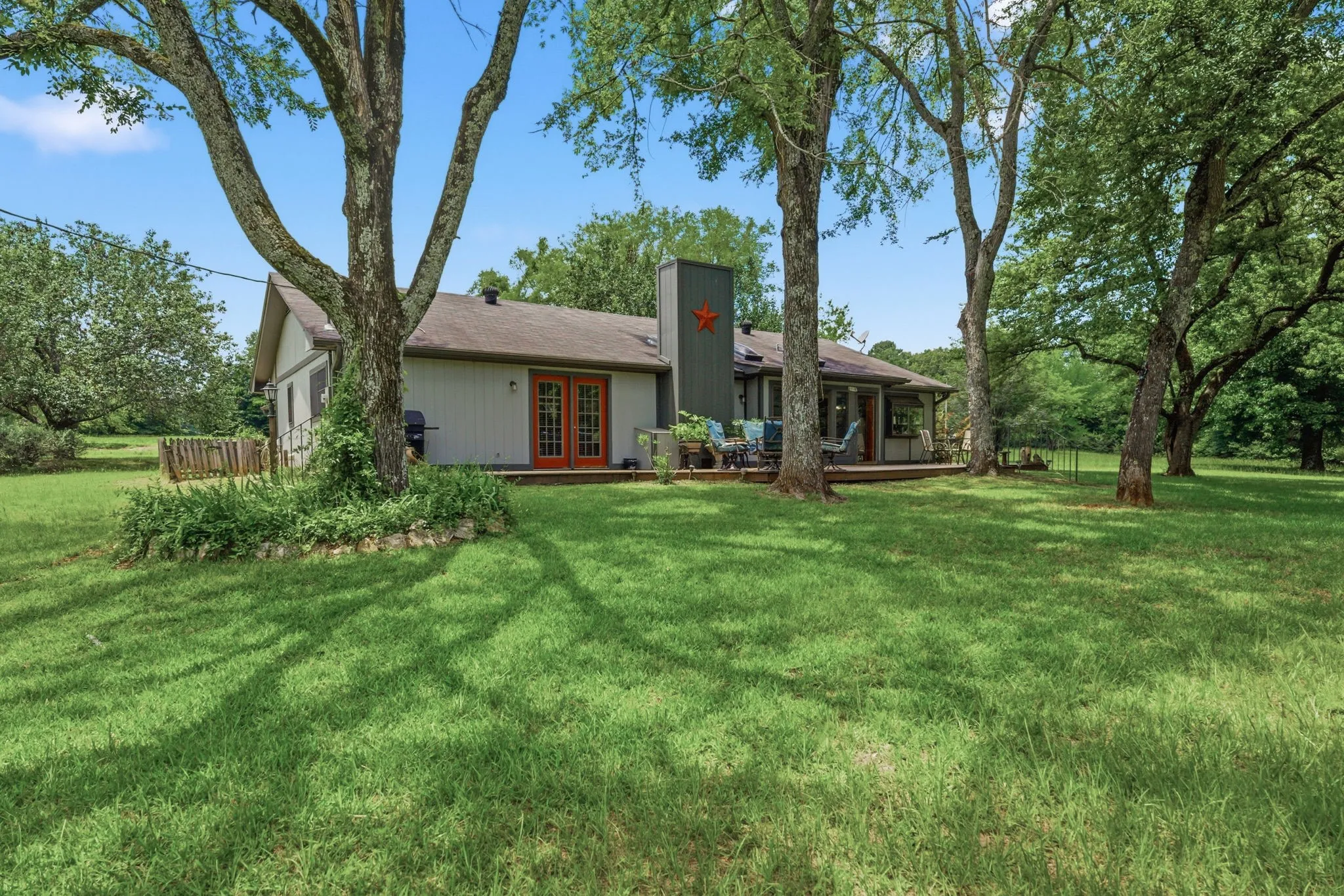 Expansive rear lawn with mature trees, a wood deck, and French doors