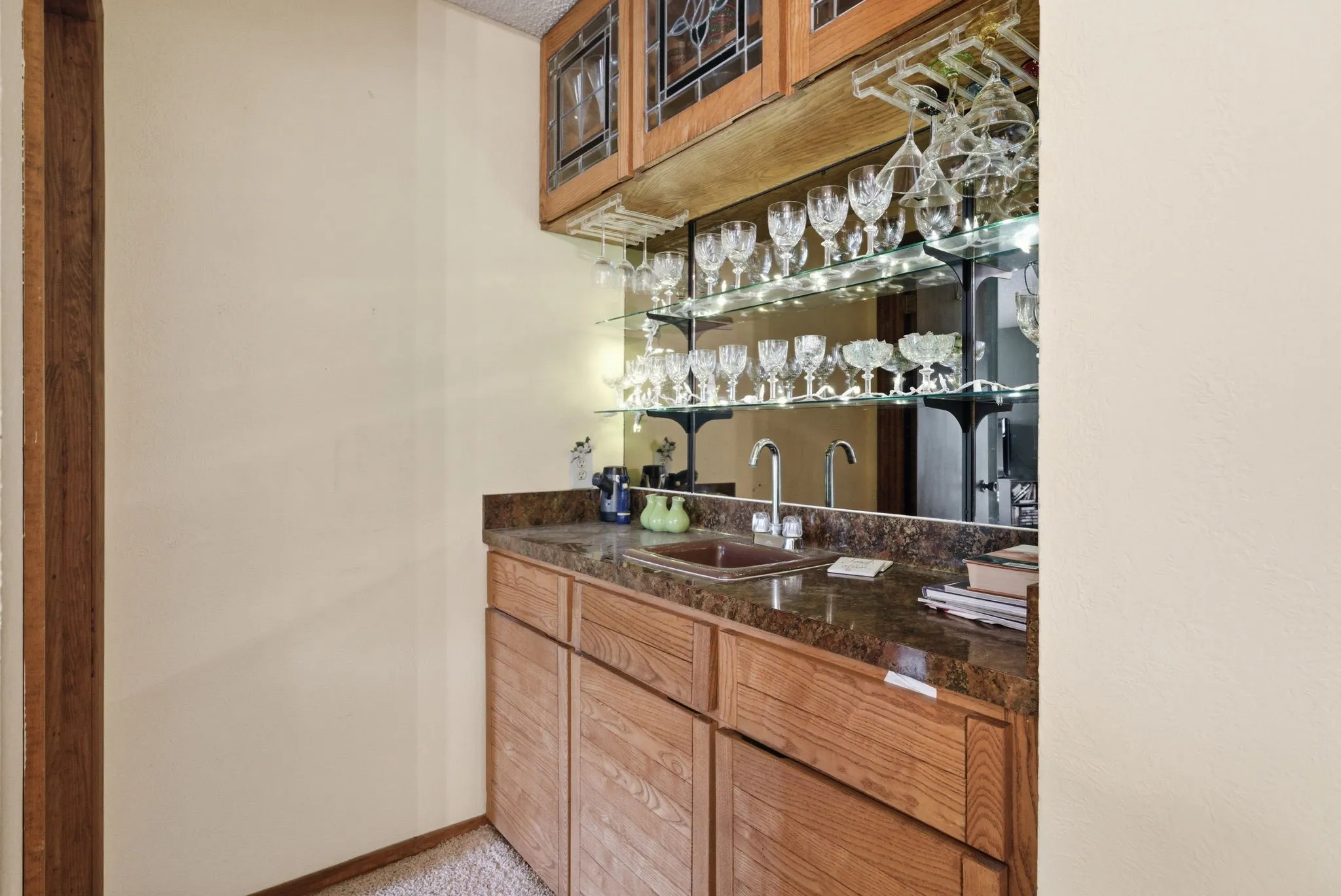 Built-in wet bar featuring a mirrored backsplash, glass shelving, and wood-finish cabinetry