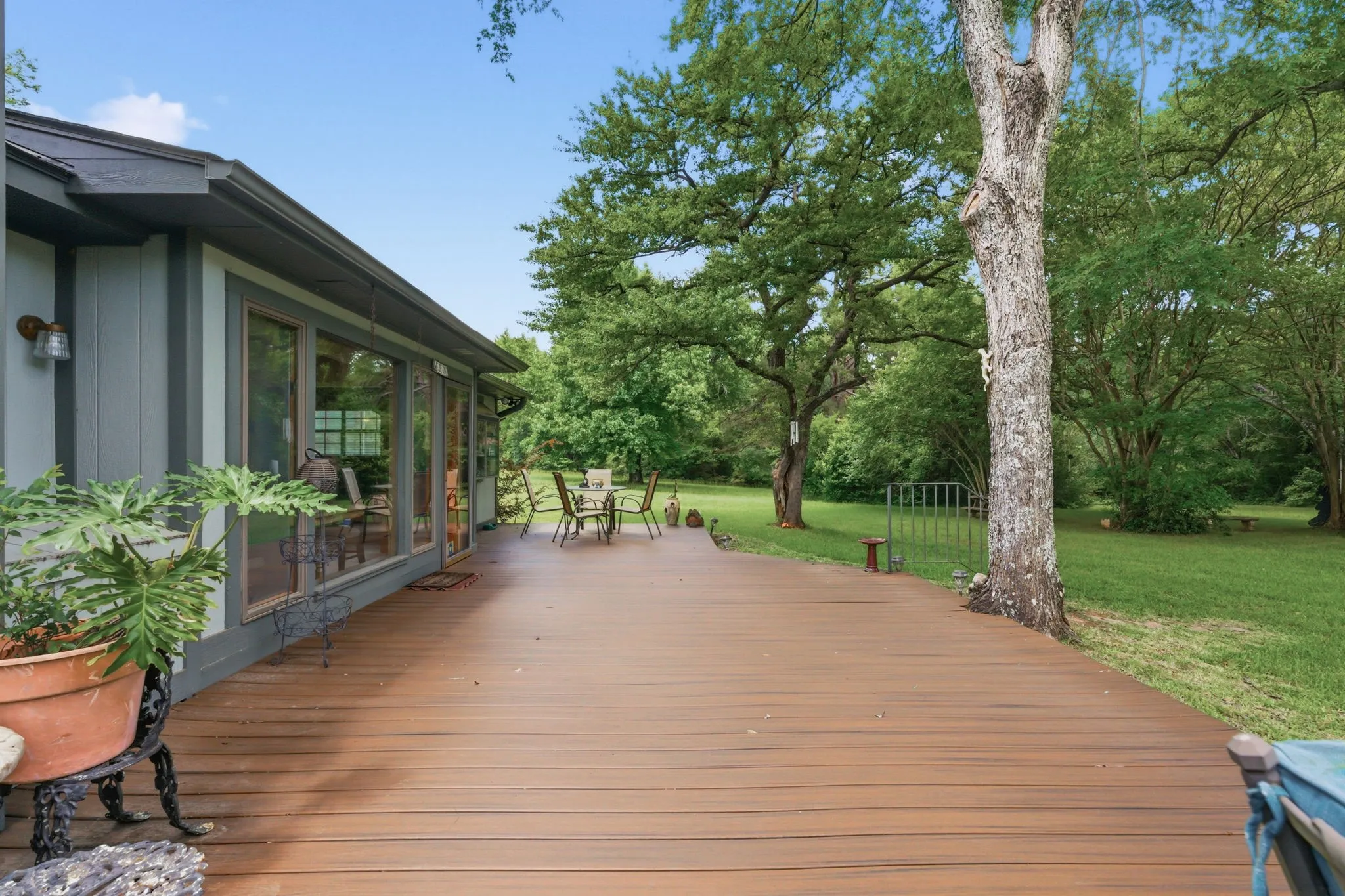 Expansive outdoor deck with wood-finish planks, bordered by mature trees and a substantial lawn area