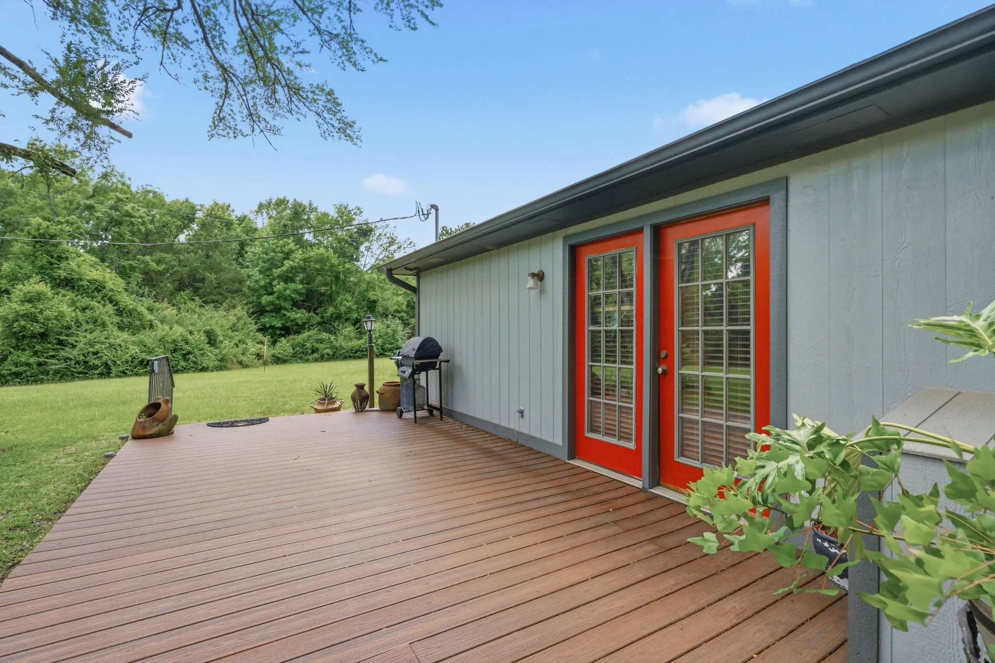 Expansive wood-finish deck with vibrant red French doors, light gray siding, and dark gray trim