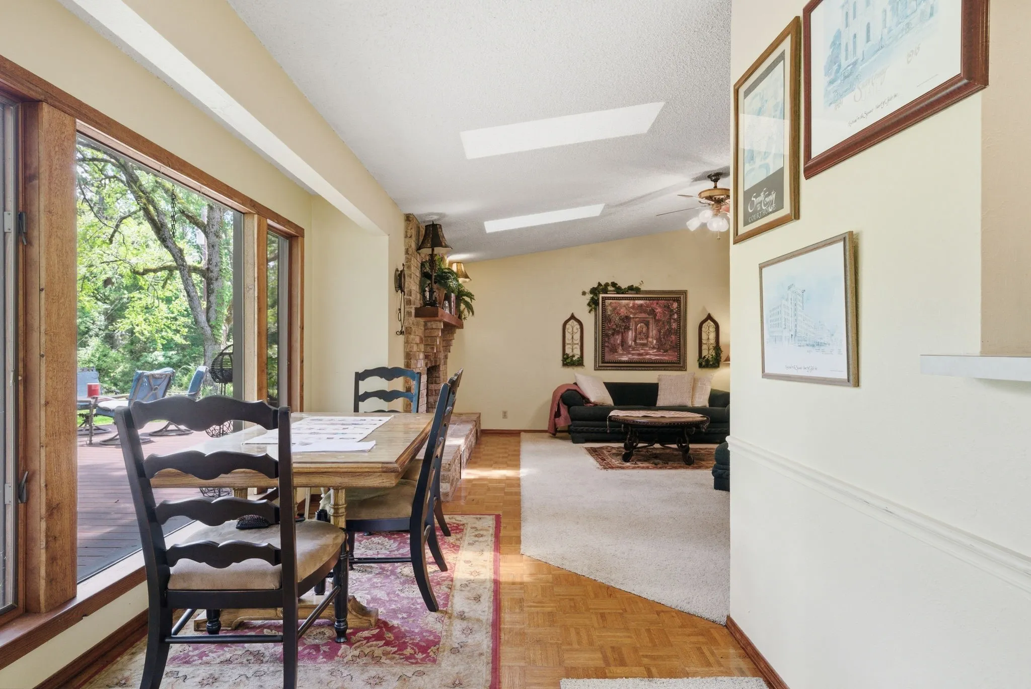 Expansive windows with wood trim, sloped ceiling with skylights, stone fireplace with hearth, and parquet wood flooring