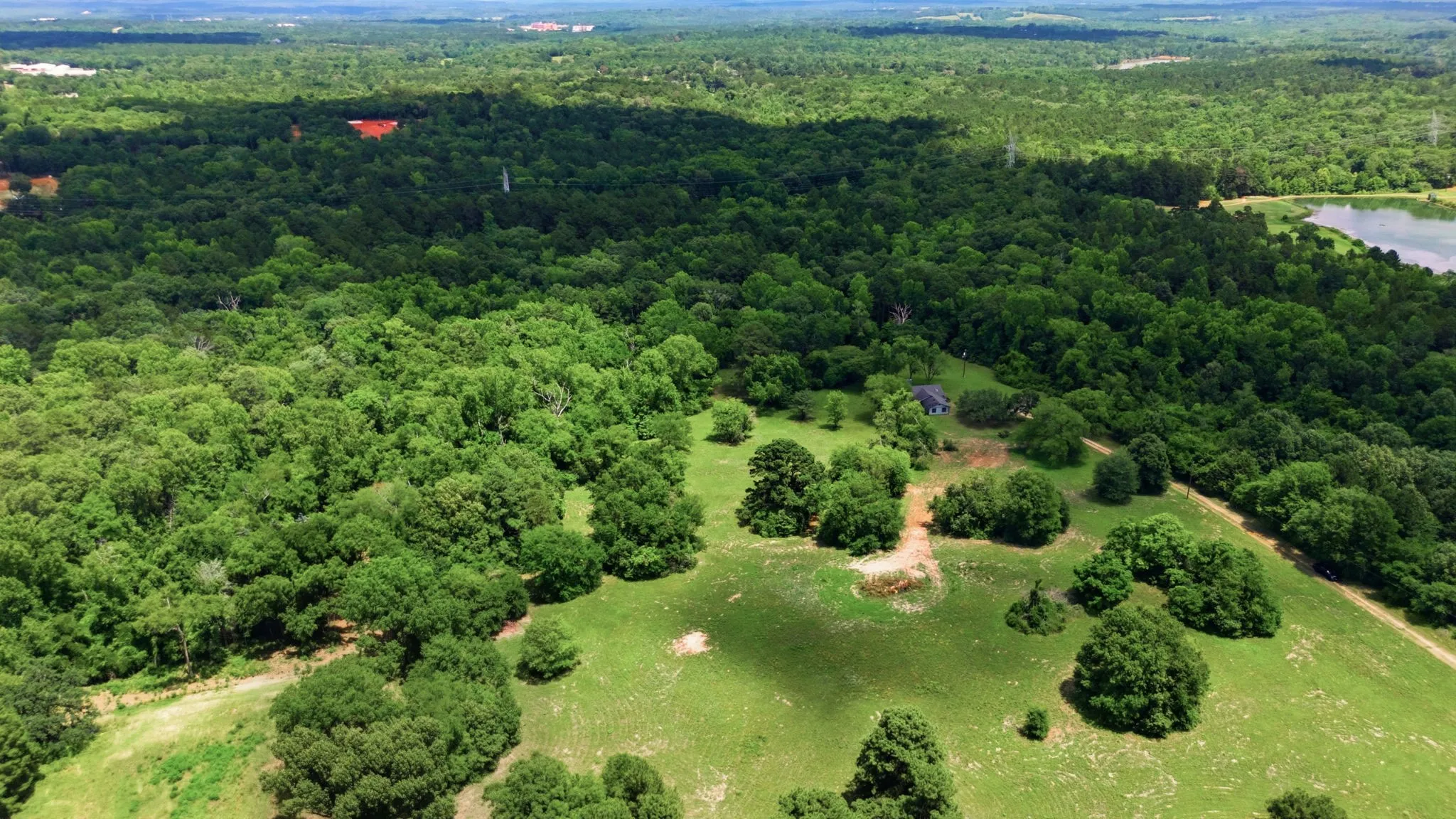 Expansive rural landscape with a residence, mature trees, and a distant body of water
