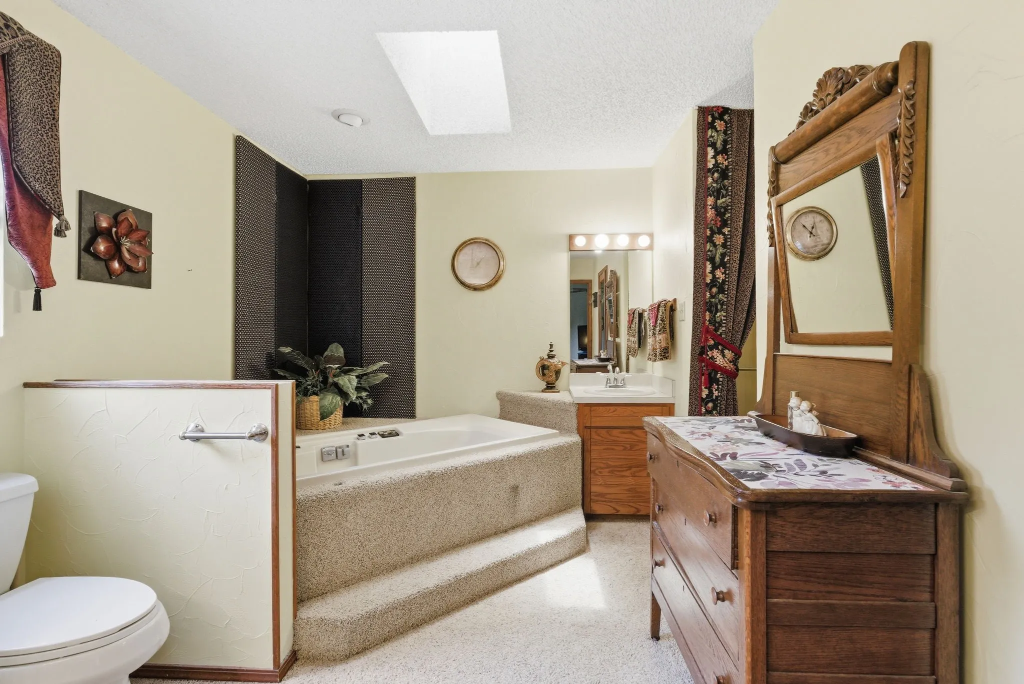 Sunken tub with carpeted steps, overhead skylight, and single vanity with a large mirror