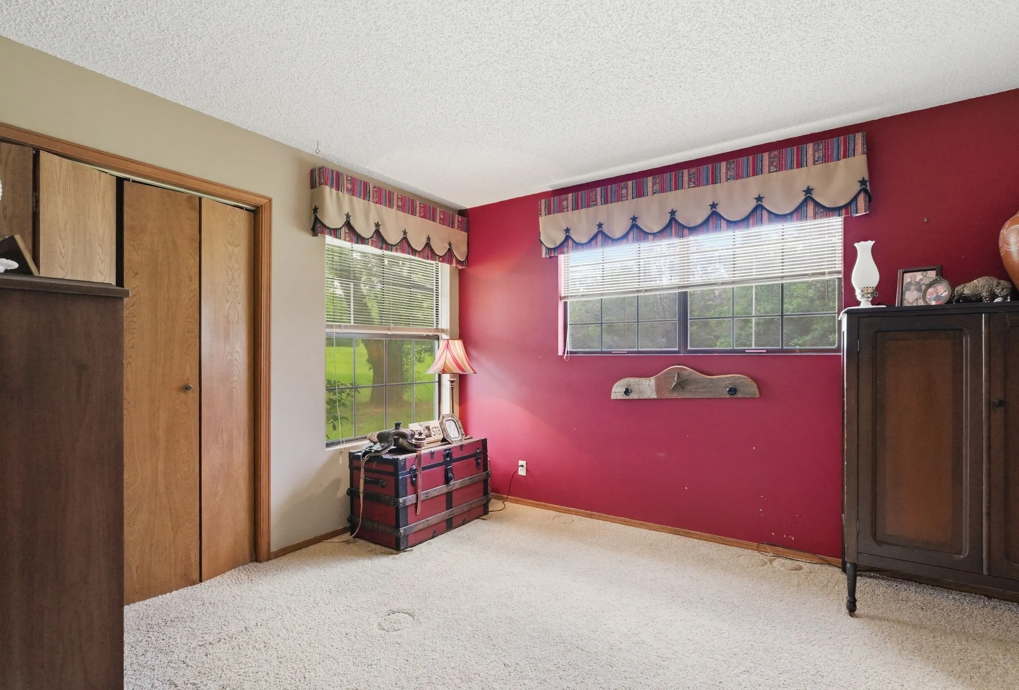 Light-colored carpeting, two windows with blinds, and wood-finish bi-fold closet doors