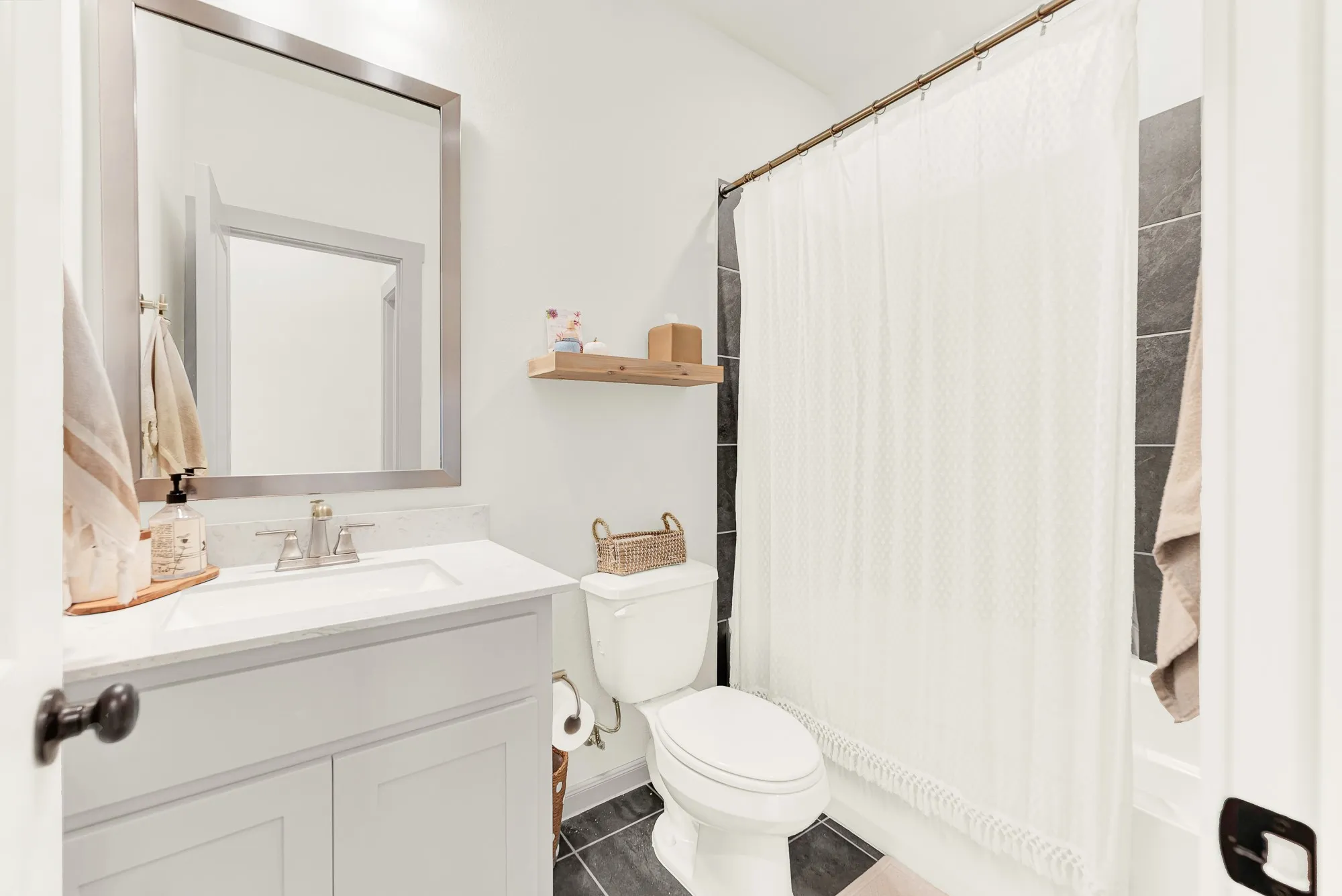 Clean white stone counters and dark floor tiles contrast beautifully under soft vanity lighting. Family members can quickly gear up for the day ahead in a bright, orderly setting.