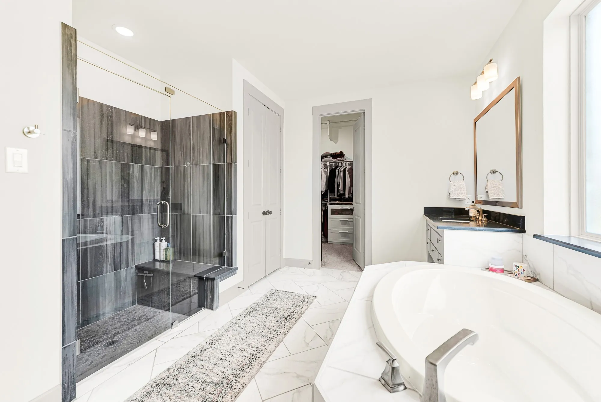 Dark vertical tilework creates bold contrast inside a glass walk-in shower set beside pristine marble counters. Imagine starting brisk morning routines with an invigorating, spa-like shower experience.