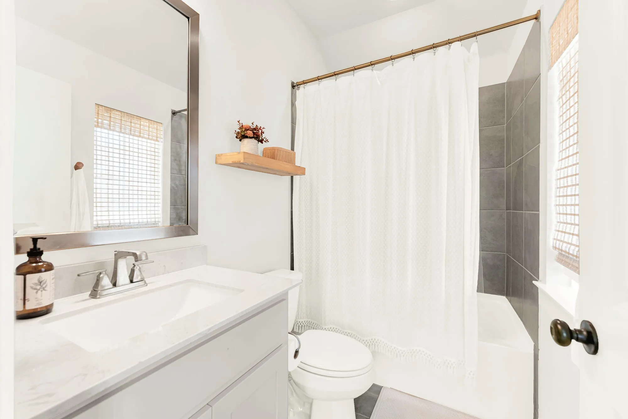 A woven window shade softens incoming sunshine beside a crisp, wide vanity mirror setup. Kids can wrap up their evening bedtime routine in a serene, organized bath space.