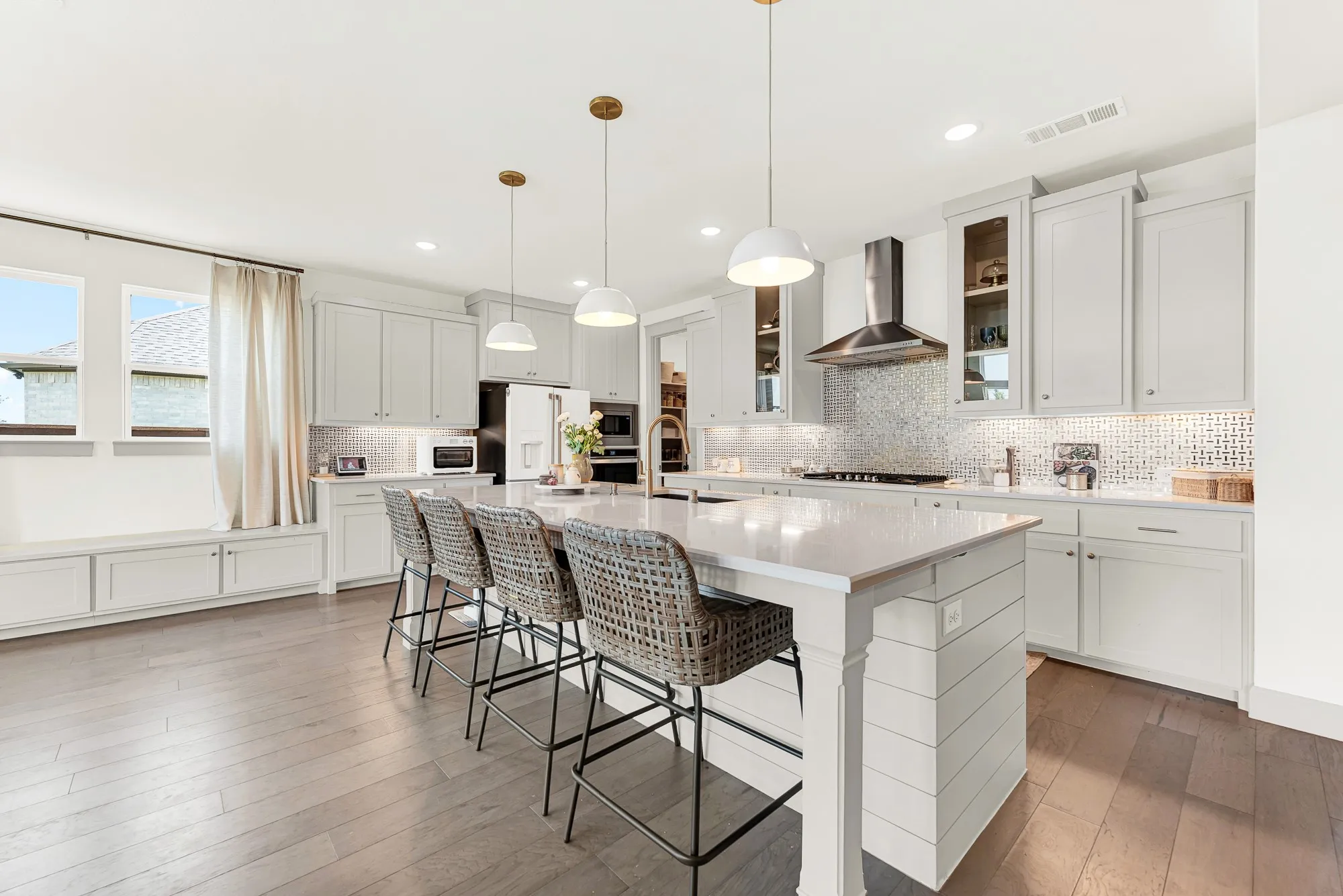 Trio pendant lights illuminate an expansive central prep island anchored by a cozy window bench. Picture lively weekend brunches where everyone gathers for warm pancakes.