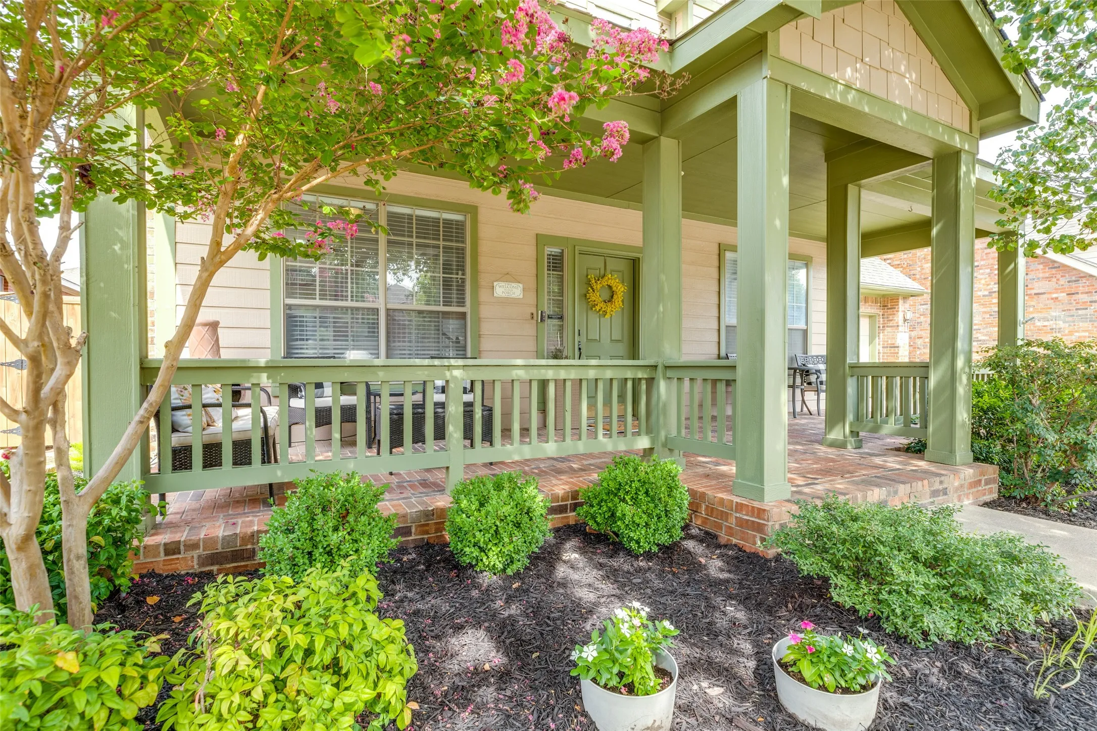 Covered brick porch with painted wood railing, square columns, and a landscaped front yard