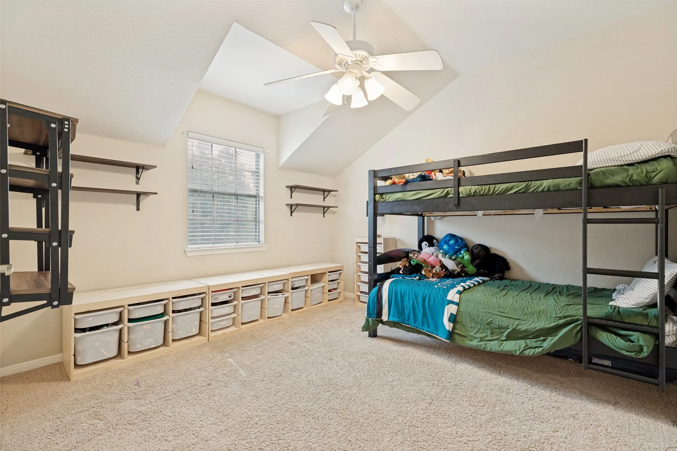 Sloped ceiling room featuring a window with blinds, built-in lower cabinetry, and wall-mounted shelving