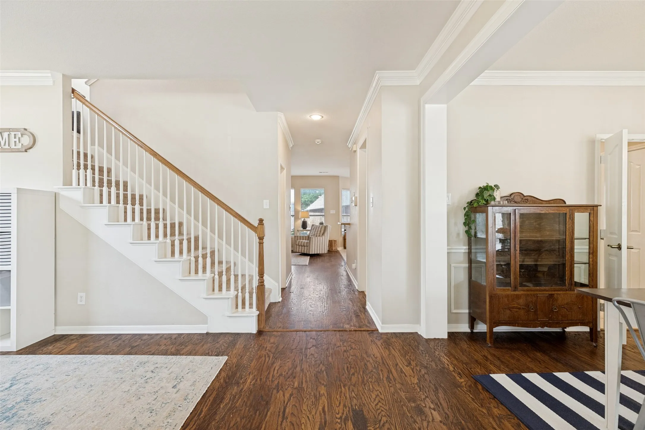 Wood-finish flooring throughout, white baluster staircase with wood handrail, crown molding, and wainscoting