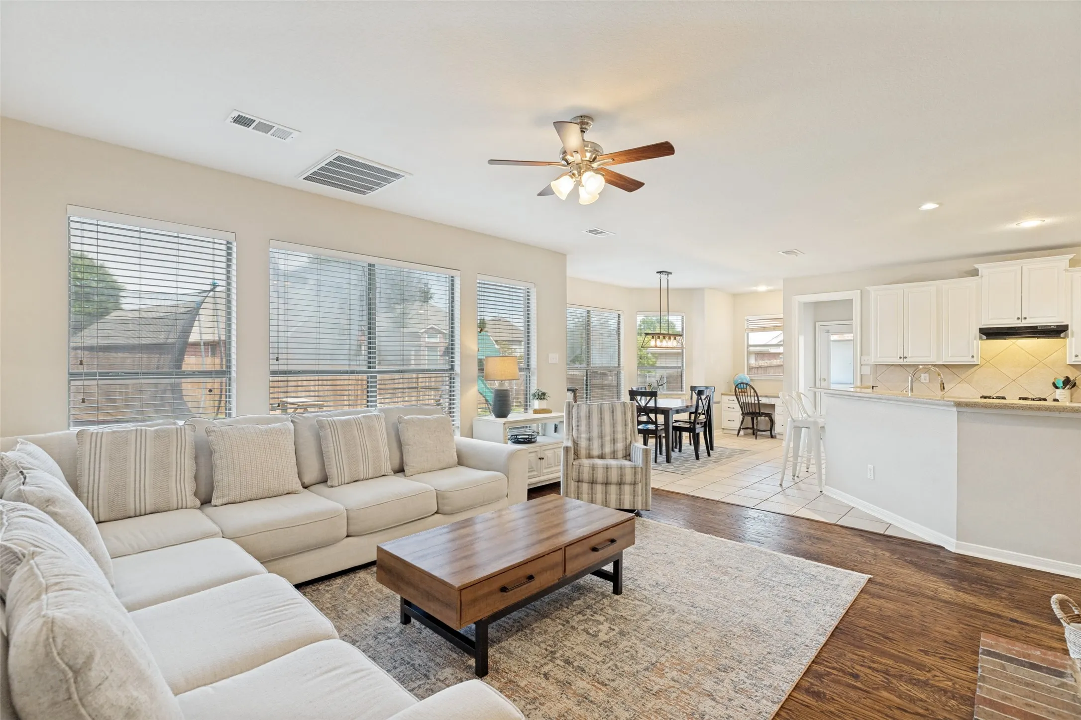 Open concept living area featuring wood-finish flooring, multiple windows with blinds, and a ceiling fan