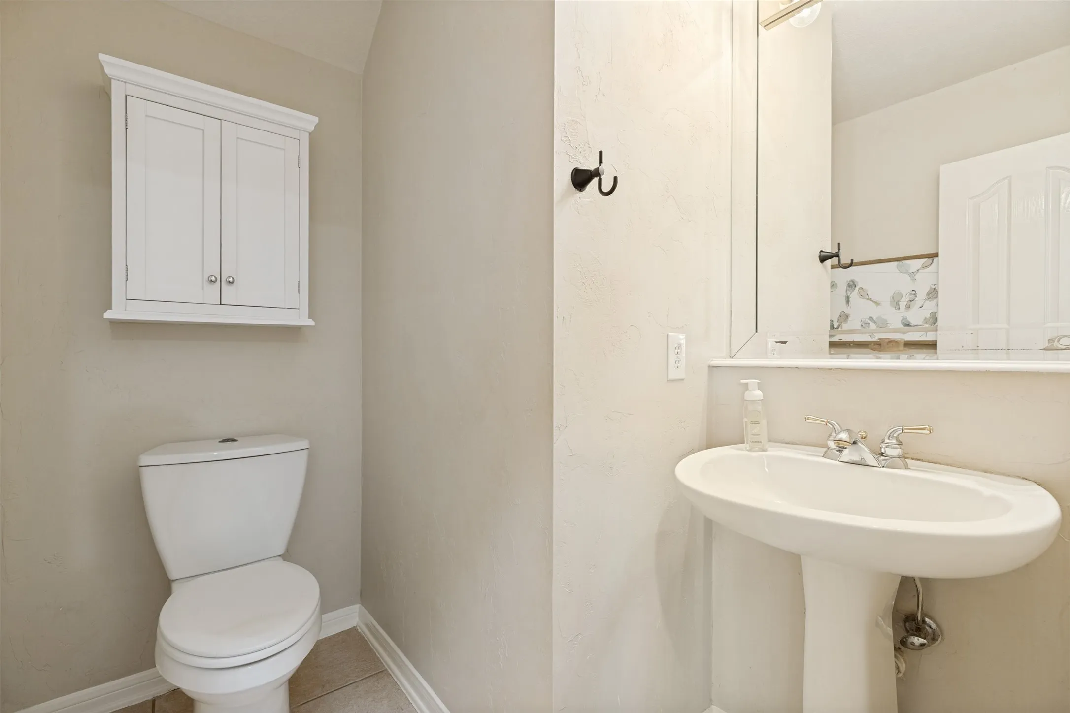 Pedestal sink with dual-handle faucet, wall-mounted mirror, and white commode