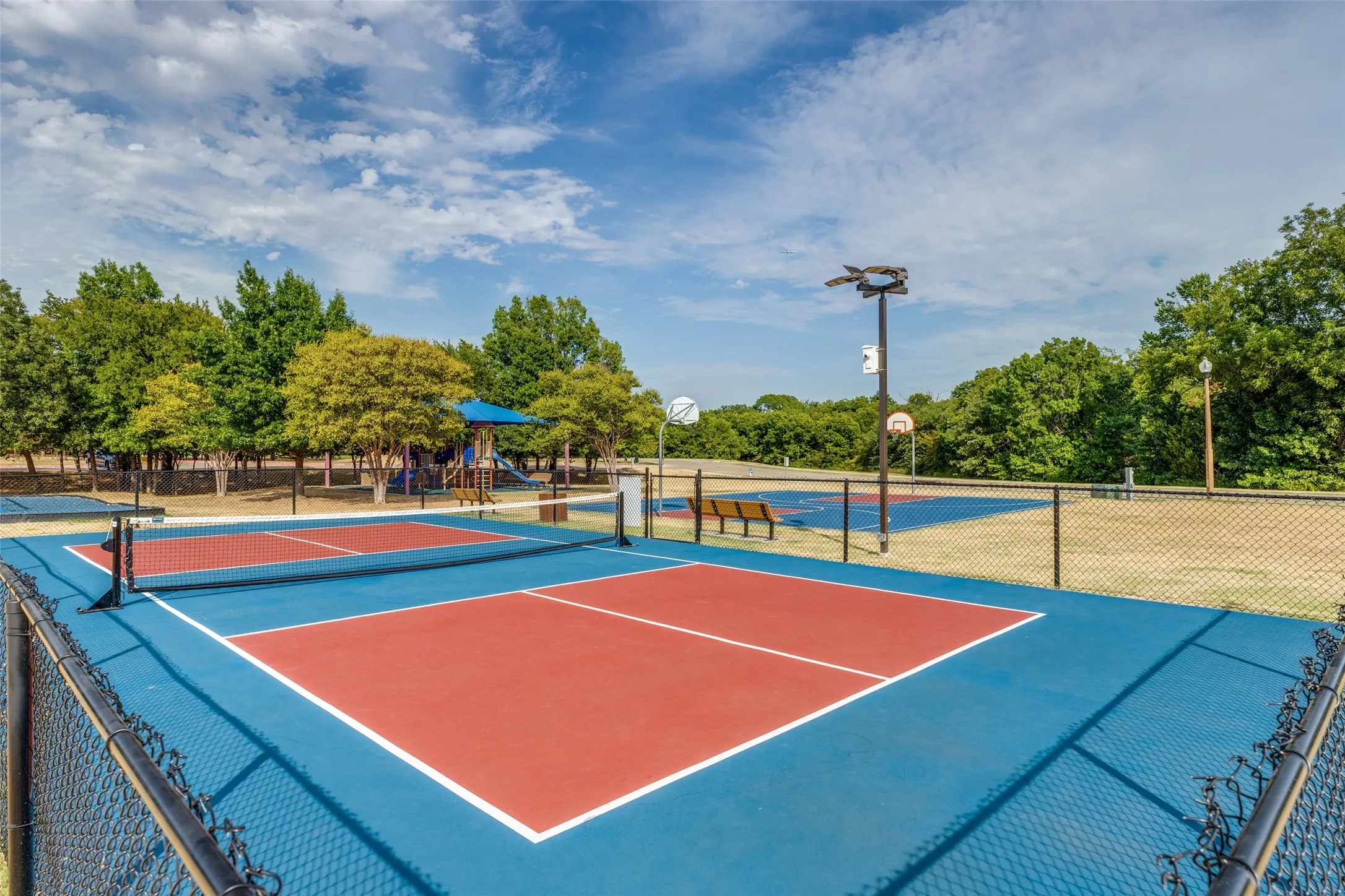 Two pickleball courts featuring blue and red playing surfaces, black fencing, and a net