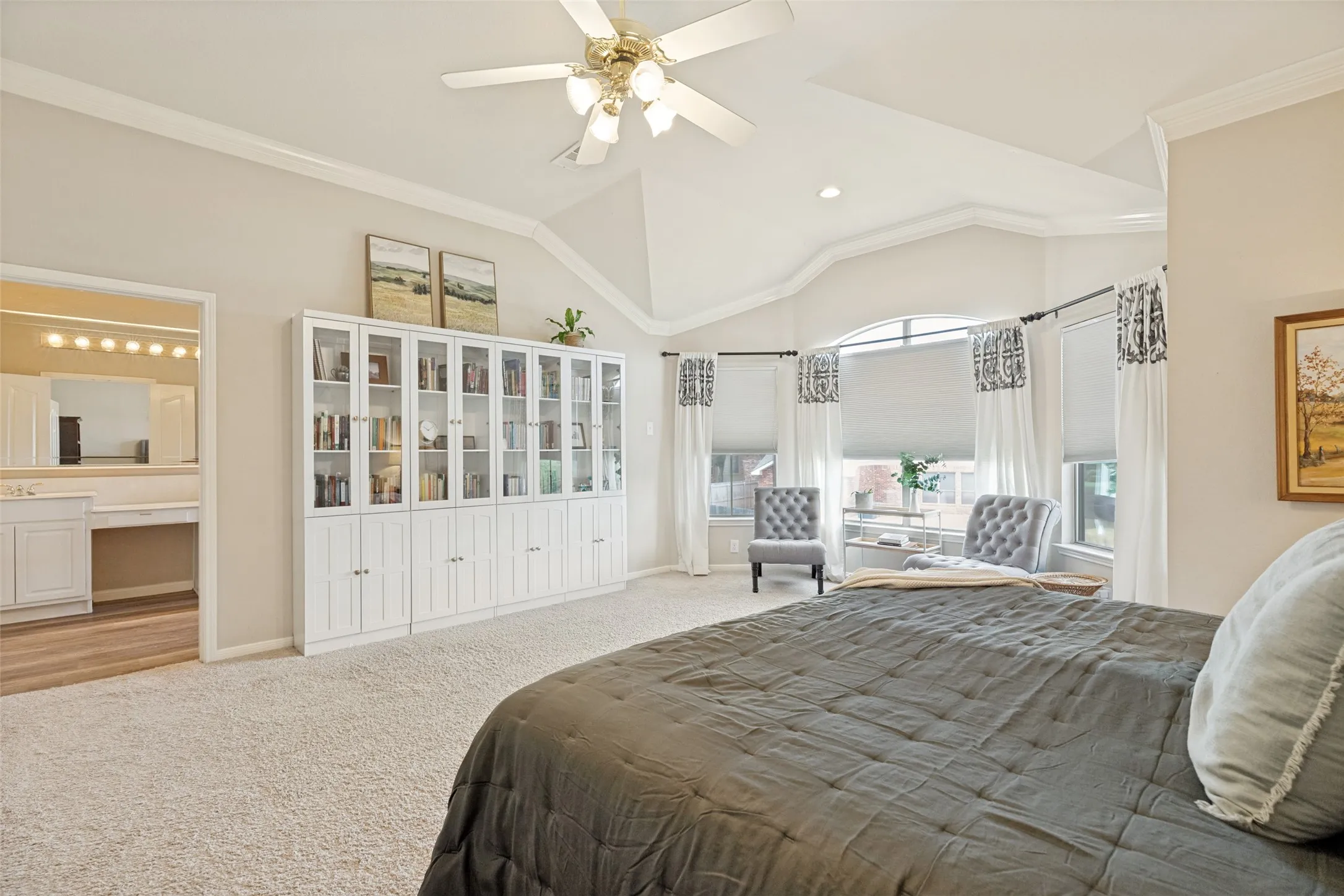 Vaulted ceiling with crown molding, built-in display cabinetry, bay window with multiple windows, and a ceiling fan with light fixture