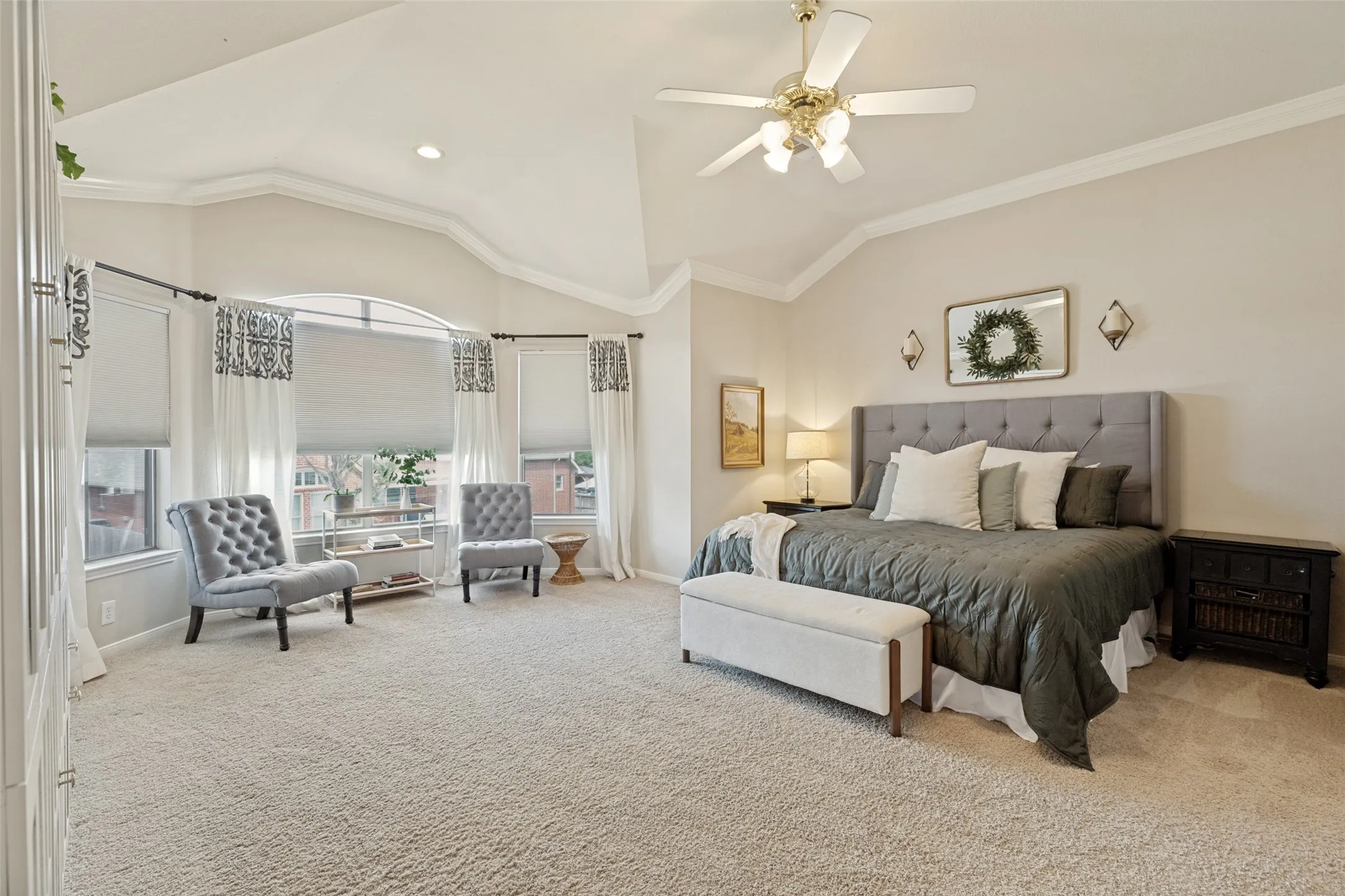 Vaulted ceilings with crown molding, bay window with arched transom, ceiling fan with integrated lighting, and carpeted flooring