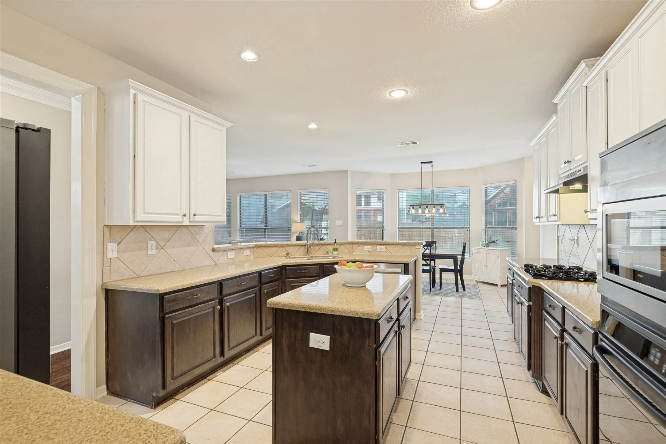 Kitchen featuring two-tone cabinetry, a central island, built-in stainless steel appliances, tile flooring, and a tile backsplash