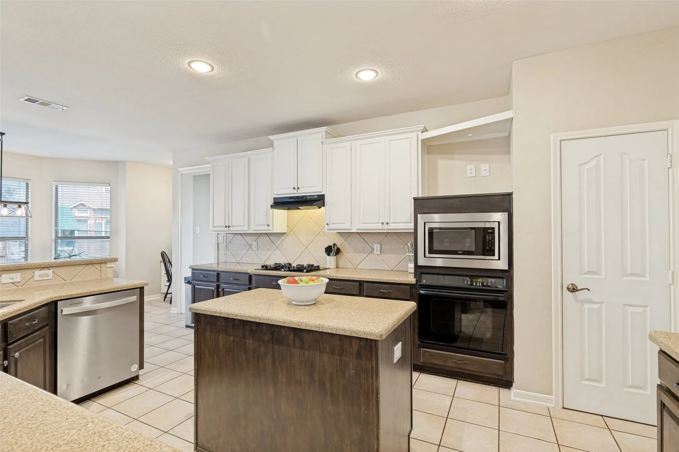 Kitchen featuring an island, light-toned countertops, white cabinetry, integrated stainless steel appliances, and tile flooring
