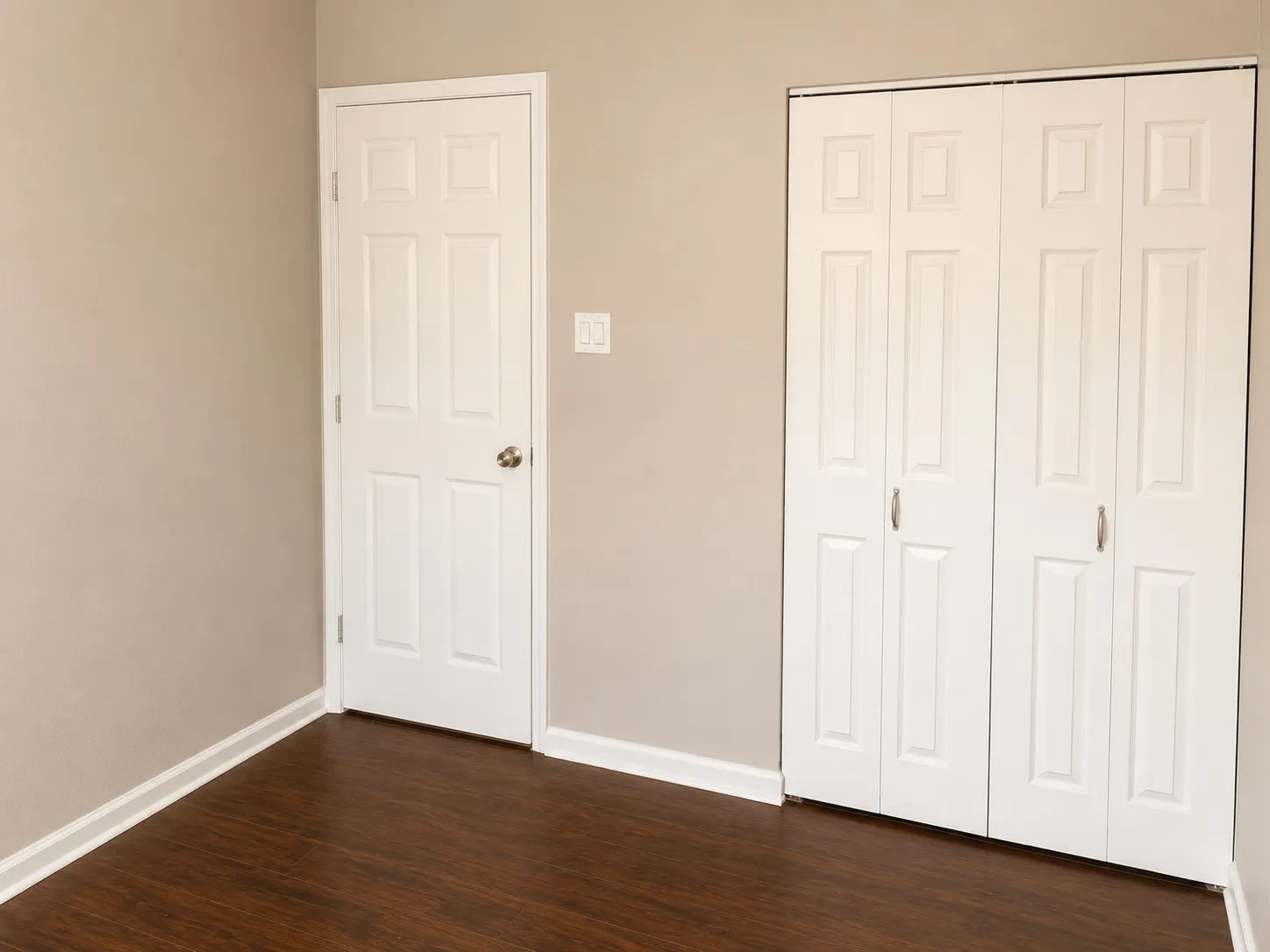 Wood-finish flooring, neutral wall paint, white trim, and white bi-fold closet doors