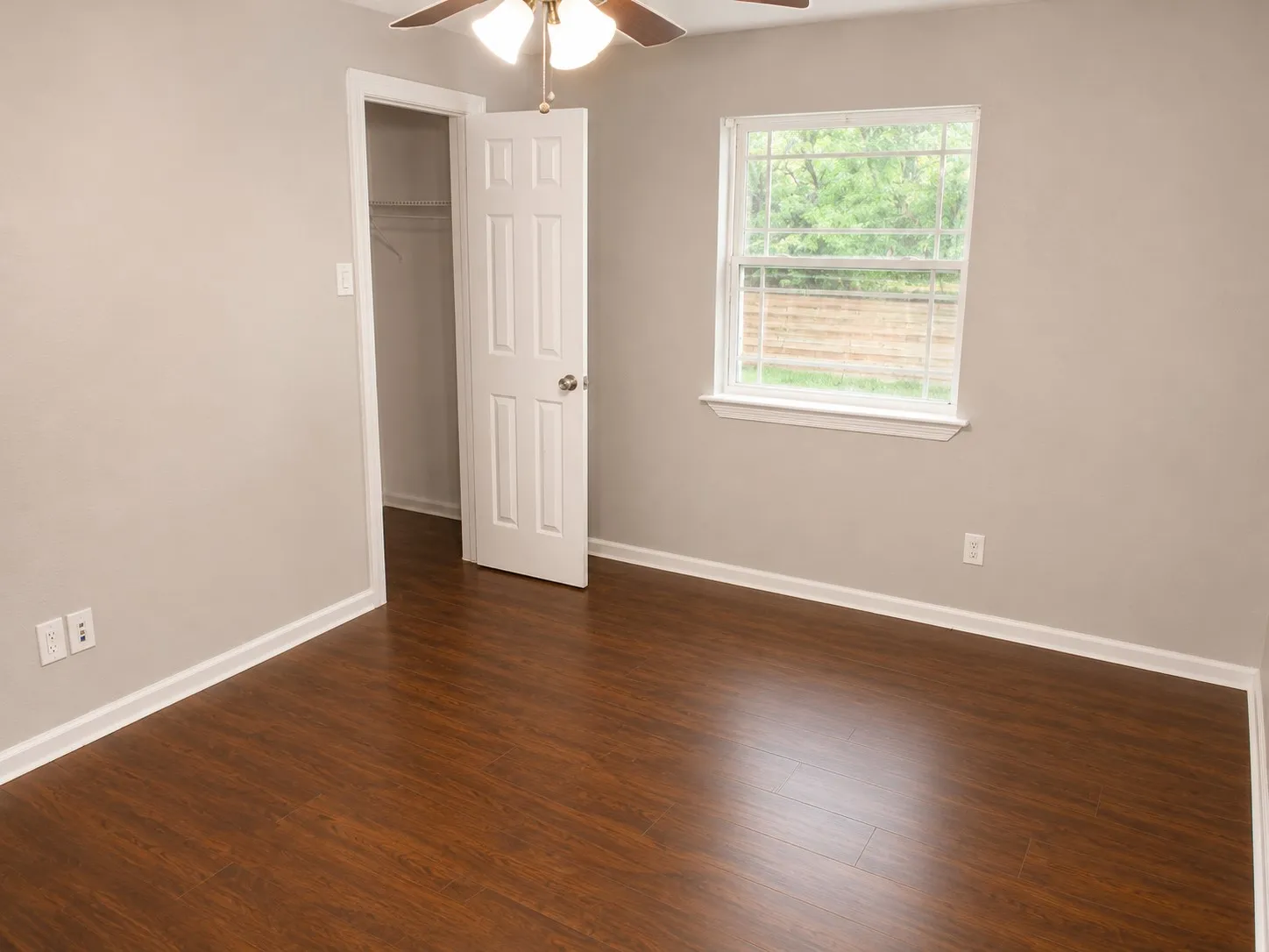 Wood-finish flooring, white trim, a ceiling fan with light fixture, and a window offering natural illumination
