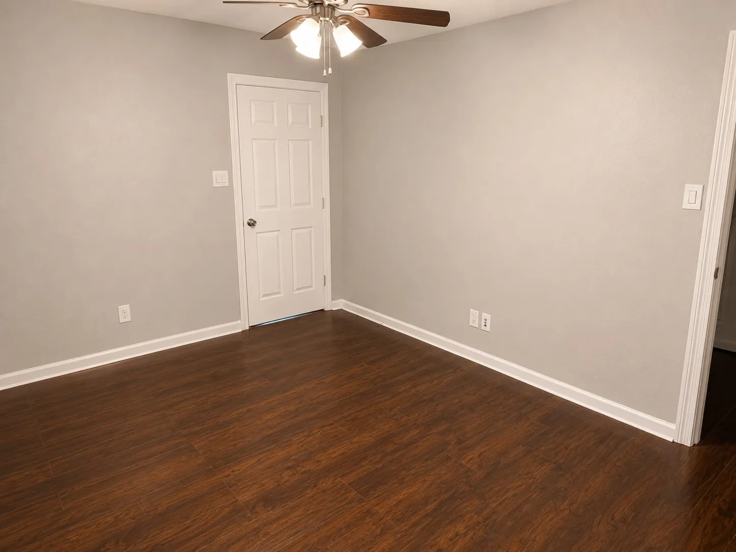 Wood-finish flooring with white trim, light gray walls, and a ceiling fan with integrated lighting