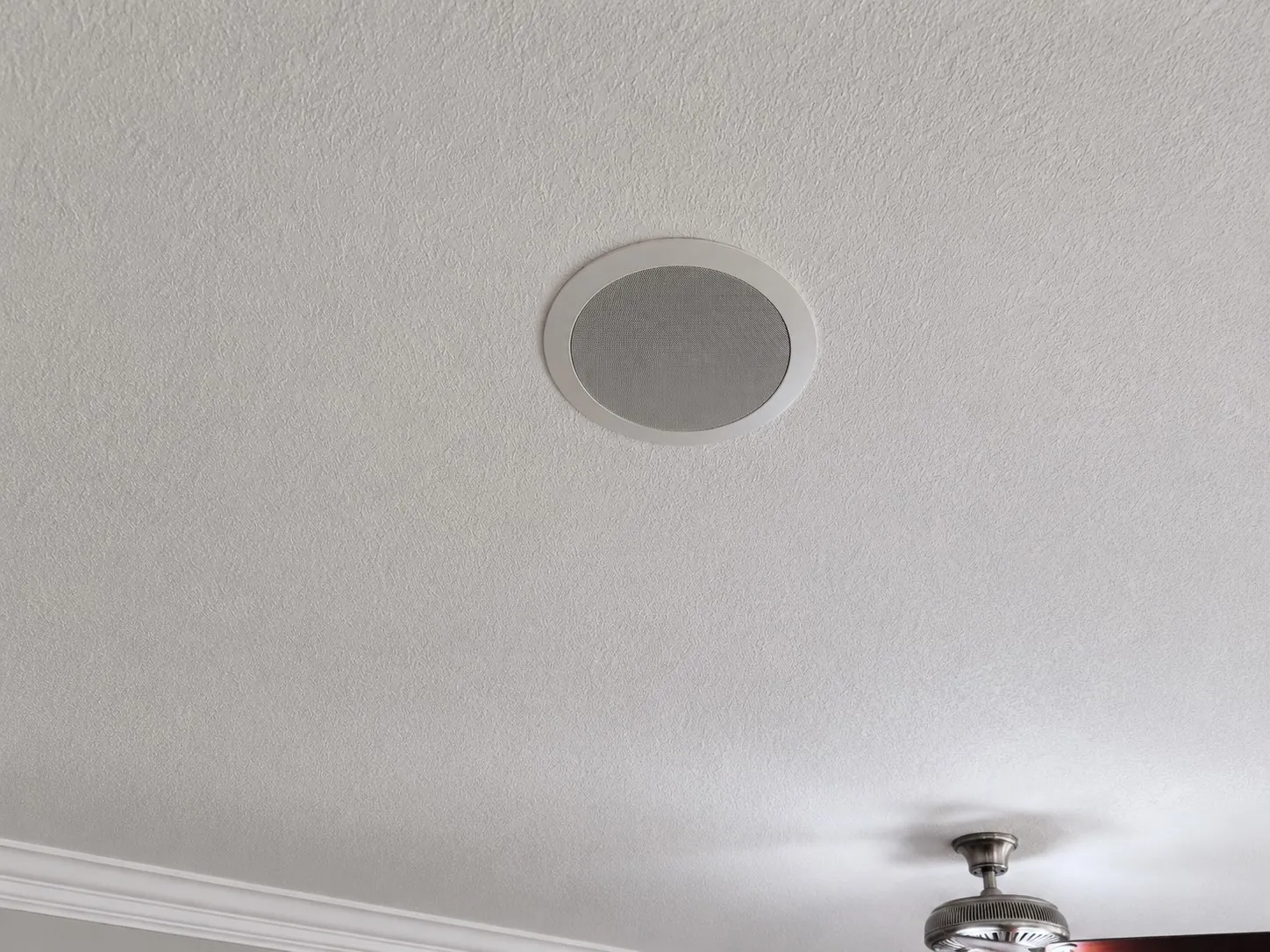 Recessed ceiling speaker, textured ceiling, crown molding, and a ceiling fan with a brushed metal finish