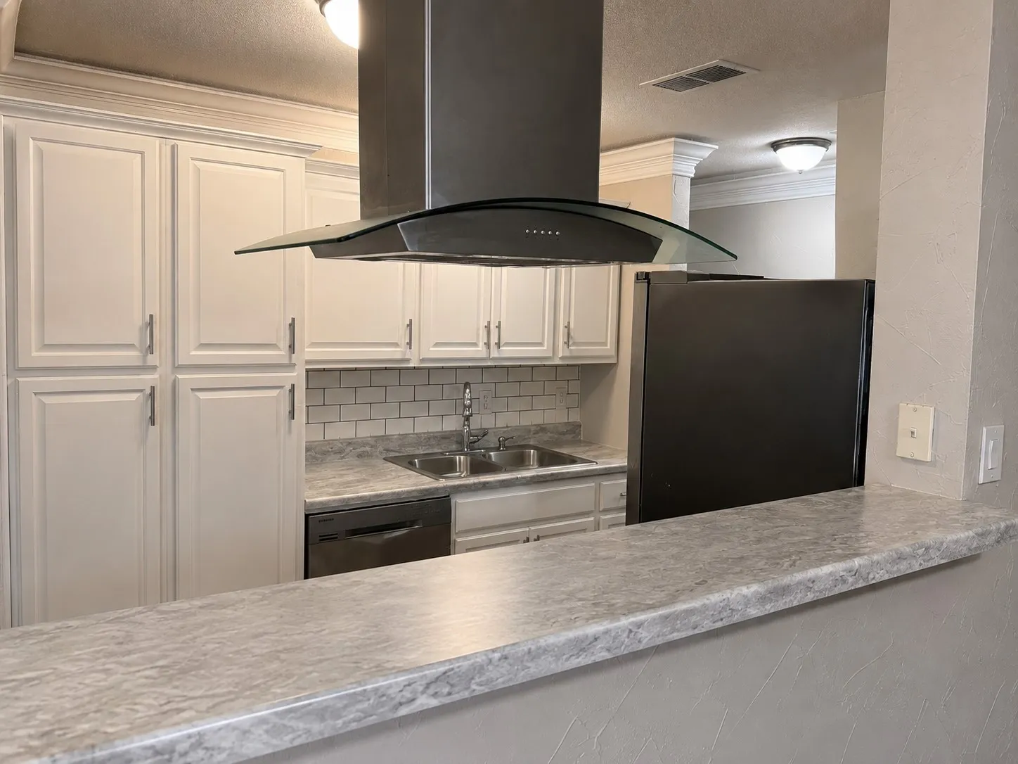 Kitchen featuring white cabinetry, subway tile backsplash, dual-basin stainless steel sink, and a modern range hood