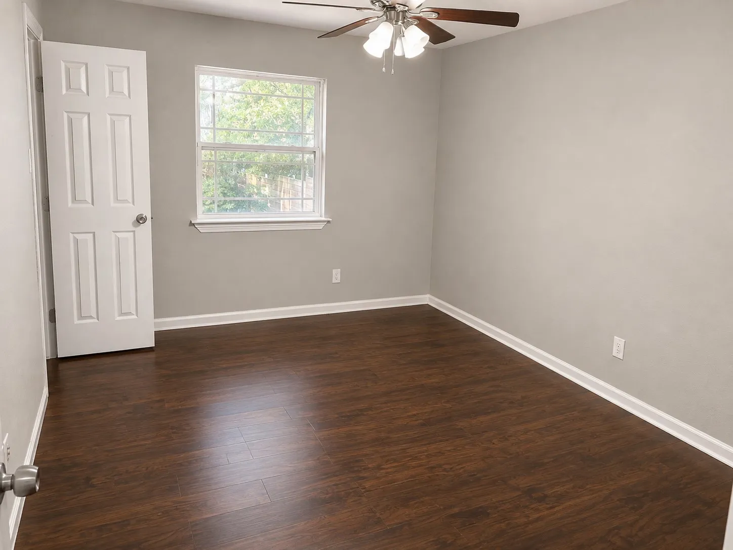 Wood-finish flooring, light gray wall paint, window with grid panes, white trim, and a ceiling fan with light fixture