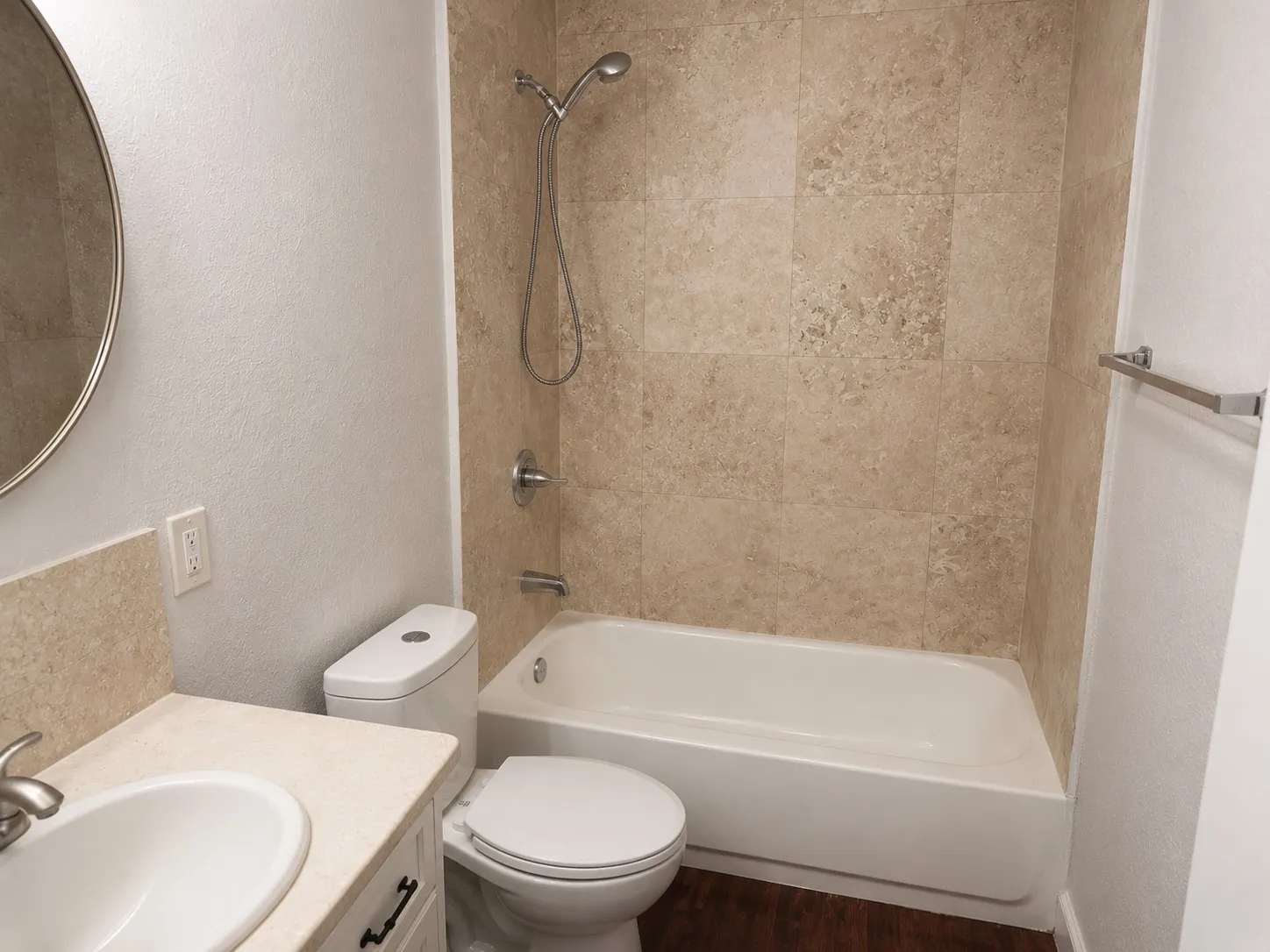 Bathroom featuring a white vanity with a built-in sink, round mirror, tiled backsplash, and a shower-over-tub combination with tiled walls