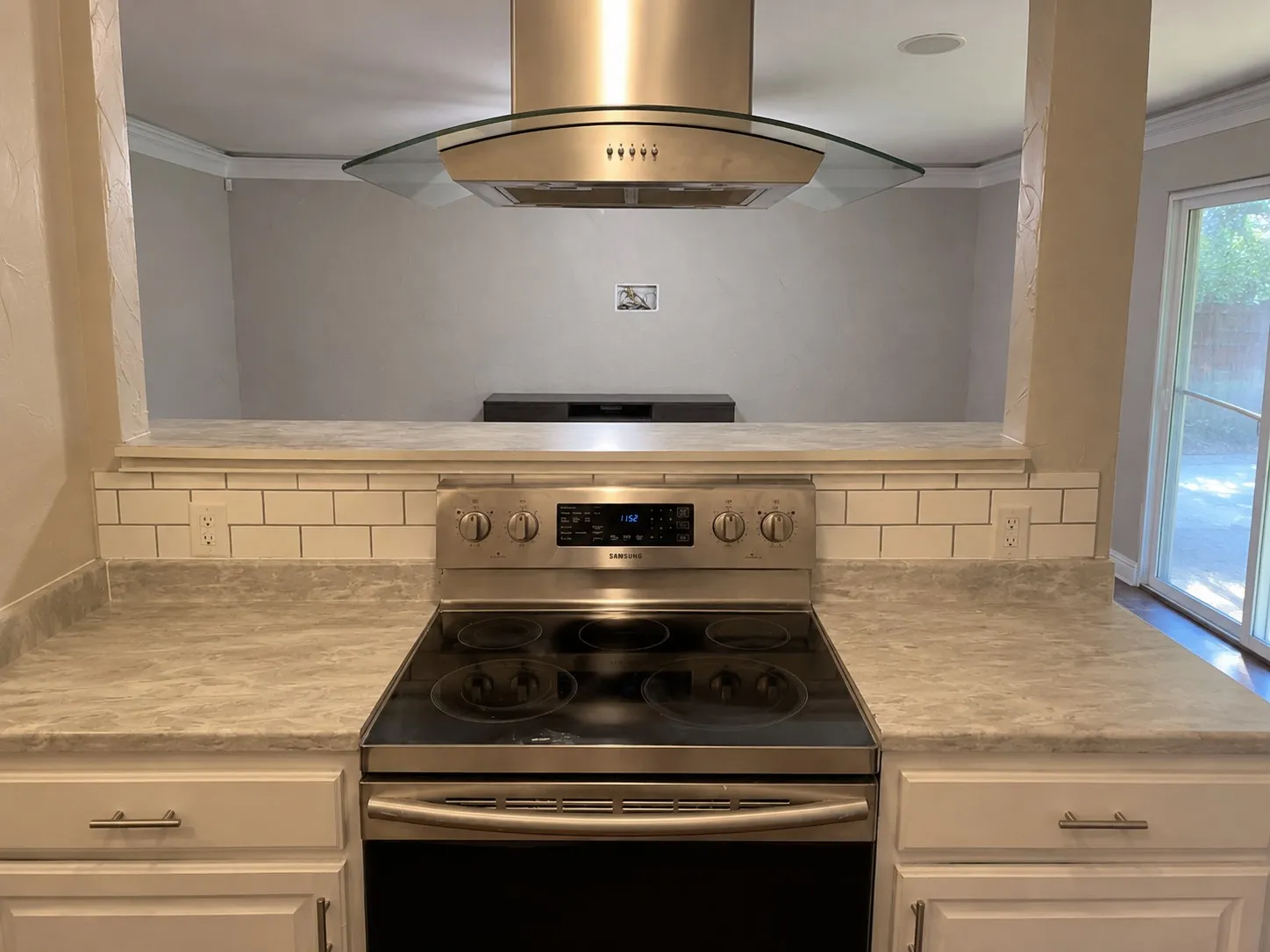 Stainless steel range with a coordinating range hood, subway tile backsplash, and light-toned countertops
