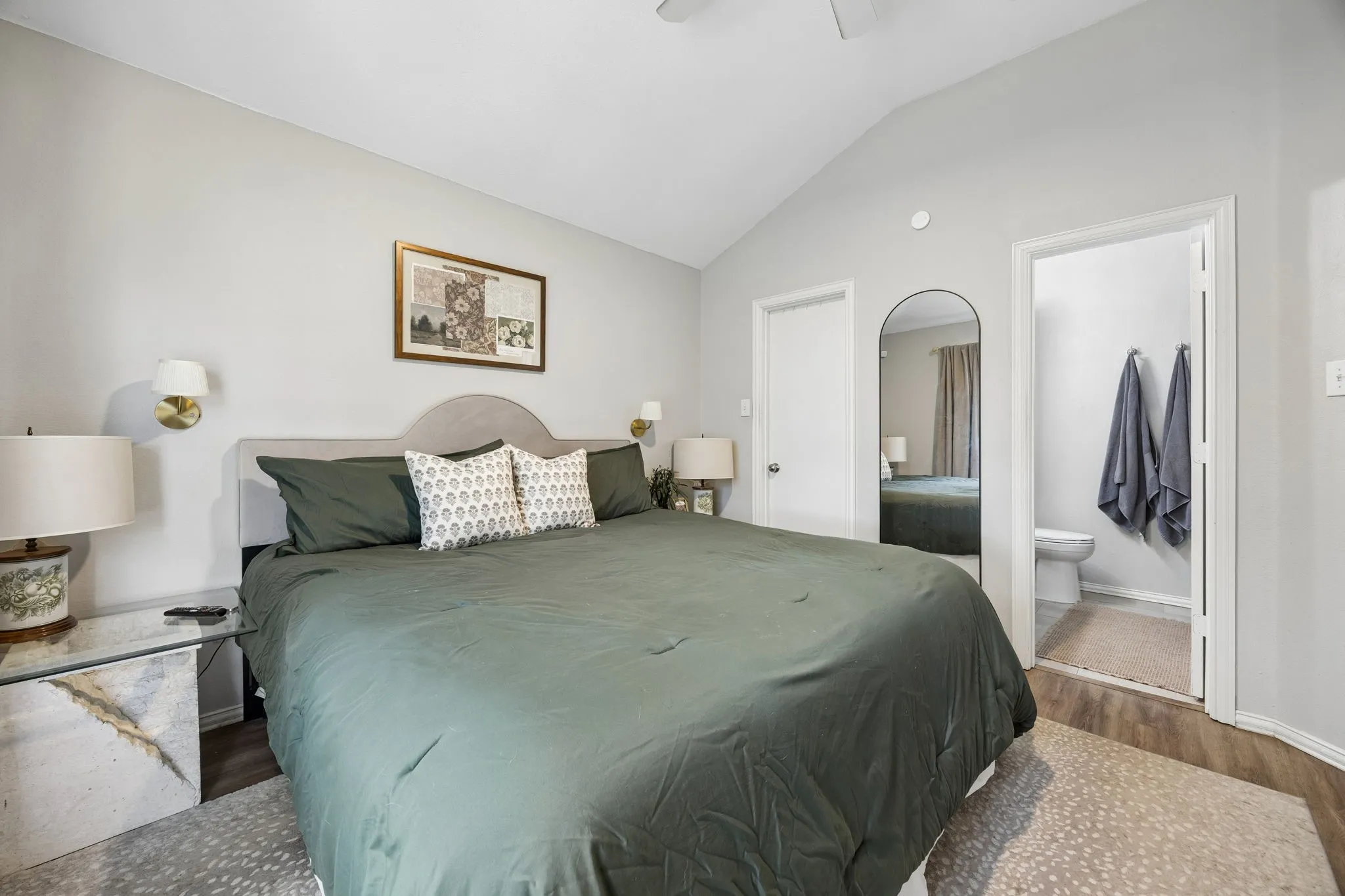 Vaulted ceiling, ceiling fan, wood-finish flooring, two wall sconces, and a full arch mirror
