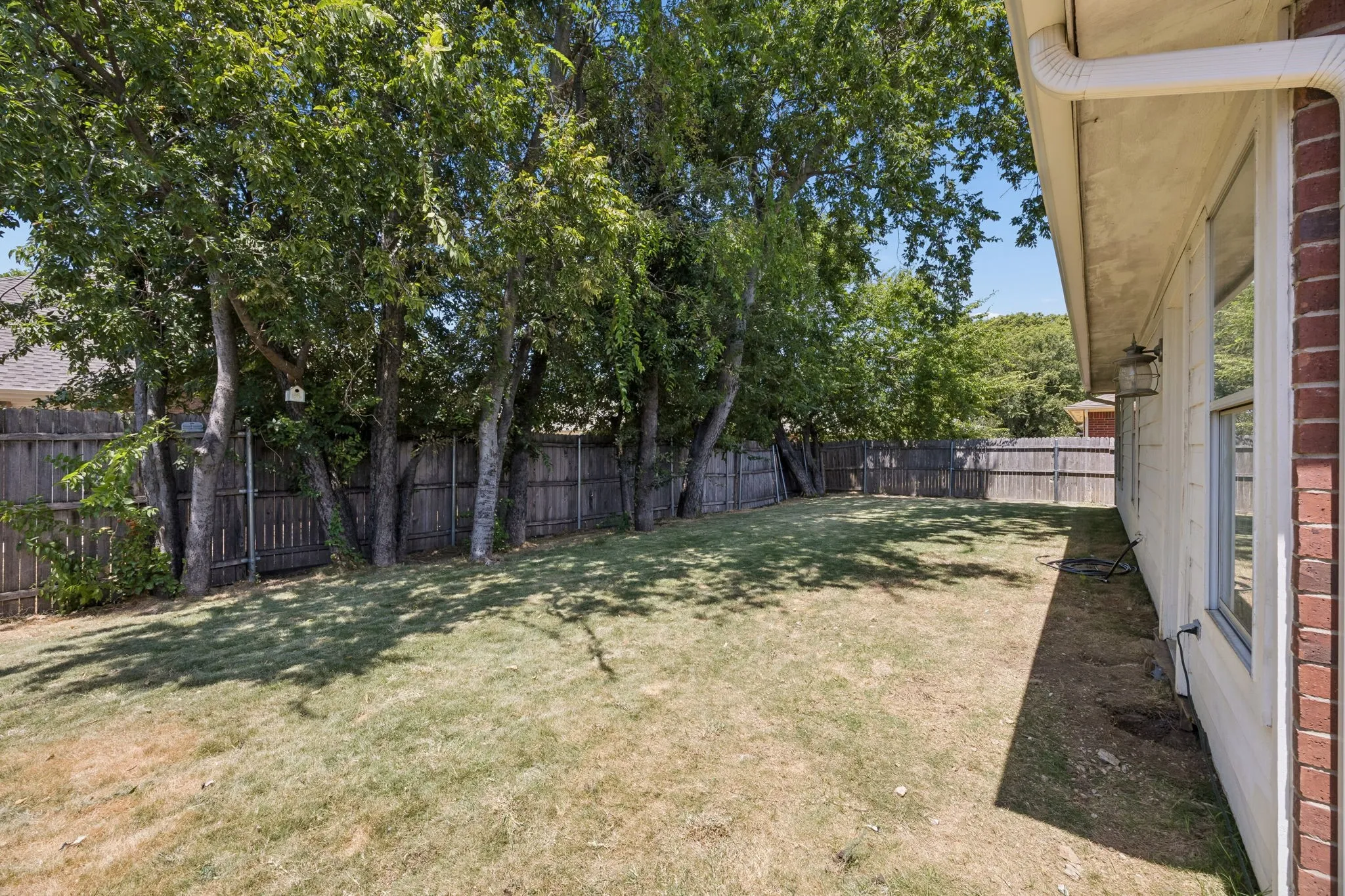 Expansive backyard featuring mature trees, wood fence, and partial brick exterior