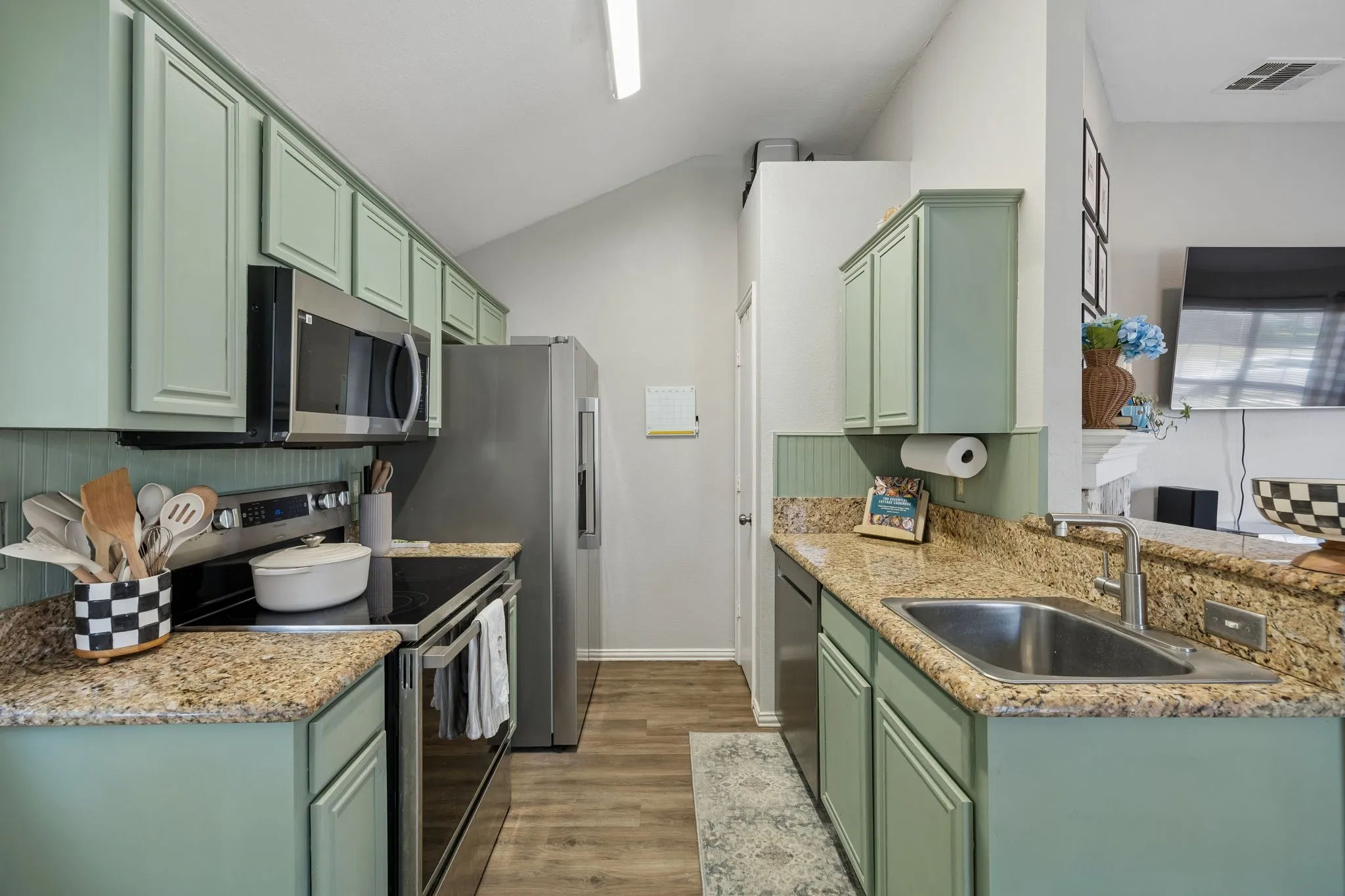 Kitchen featuring green cabinetry, granite-style countertops, stainless steel appliances, a stainless steel sink, and wood-finish flooring