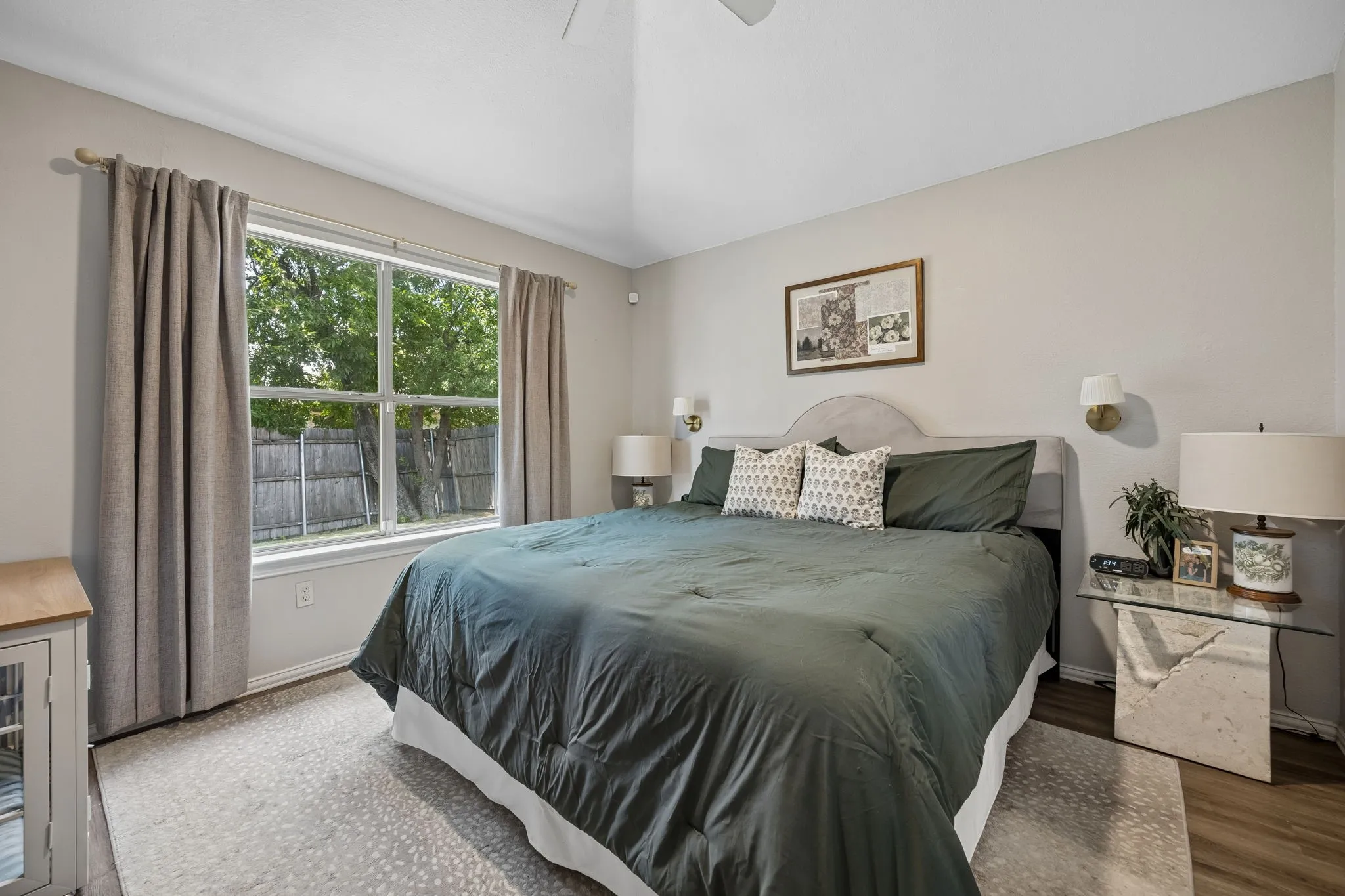 Vaulted ceiling, ceiling fan, large window with ample natural light, sconce lighting, wood-finish flooring