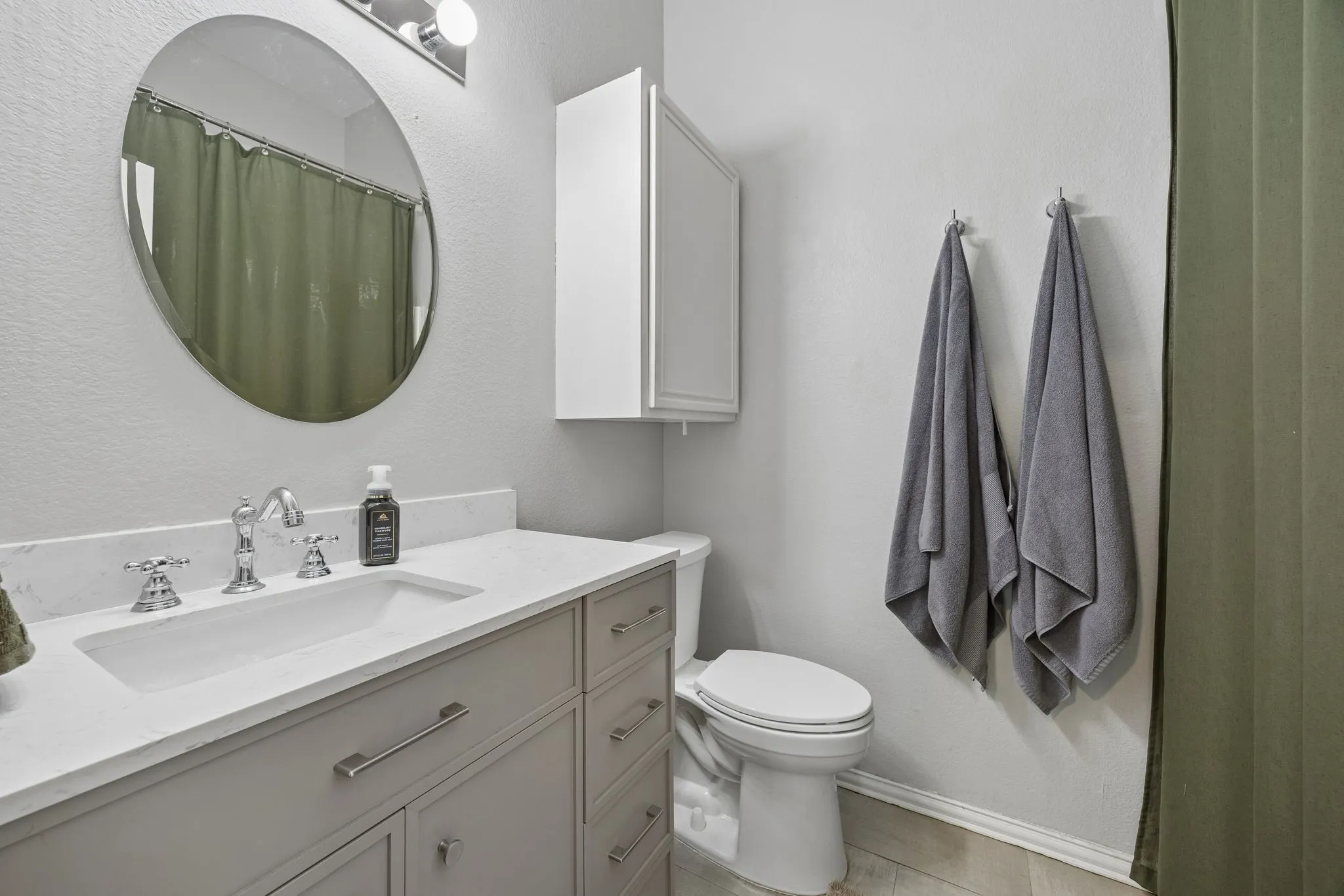 Vanity with an integrated rectangular sink, chrome hardware, oval mirror, wall-mounted storage cabinet, and a white toilet