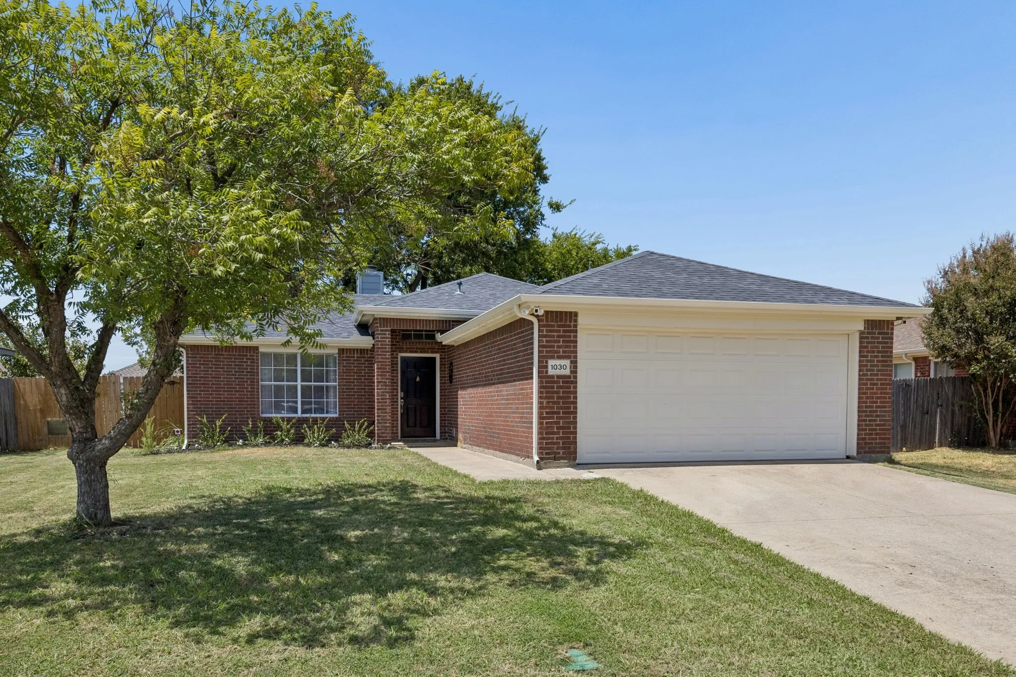 Brick exterior with a dark-shingled roof, attached garage, and a concrete driveway