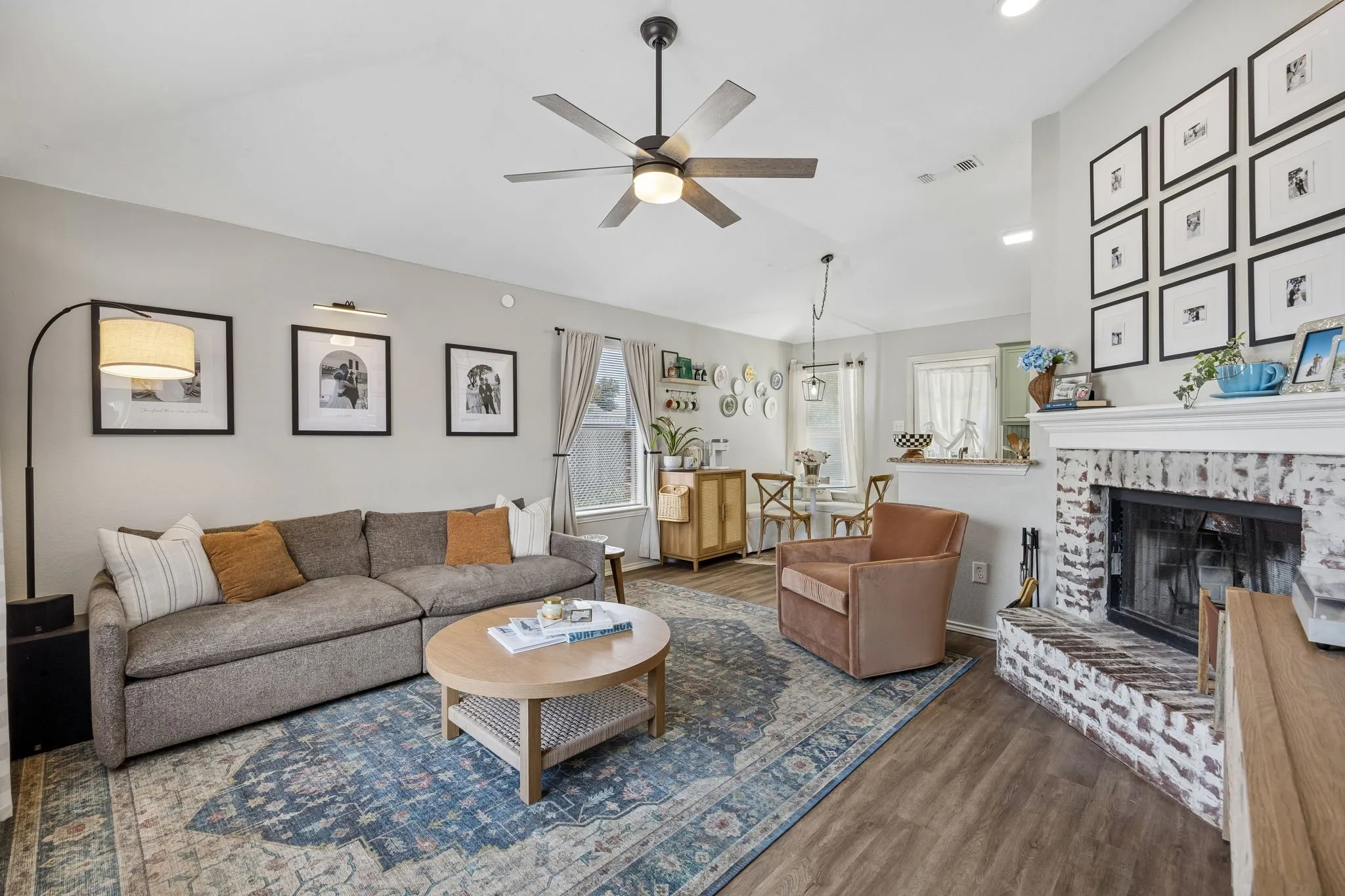 Vaulted ceilings with a ceiling fan, wood-finish flooring, and a whitewashed brick fireplace with a mantel