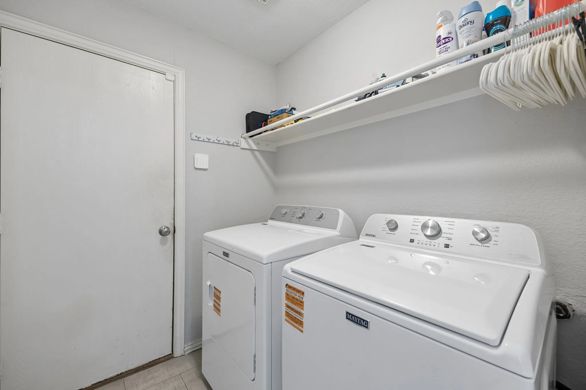 Integrated utility space featuring a white top-load washer, a white front-load dryer, and an overhead storage shelf with an integrated hanging rod