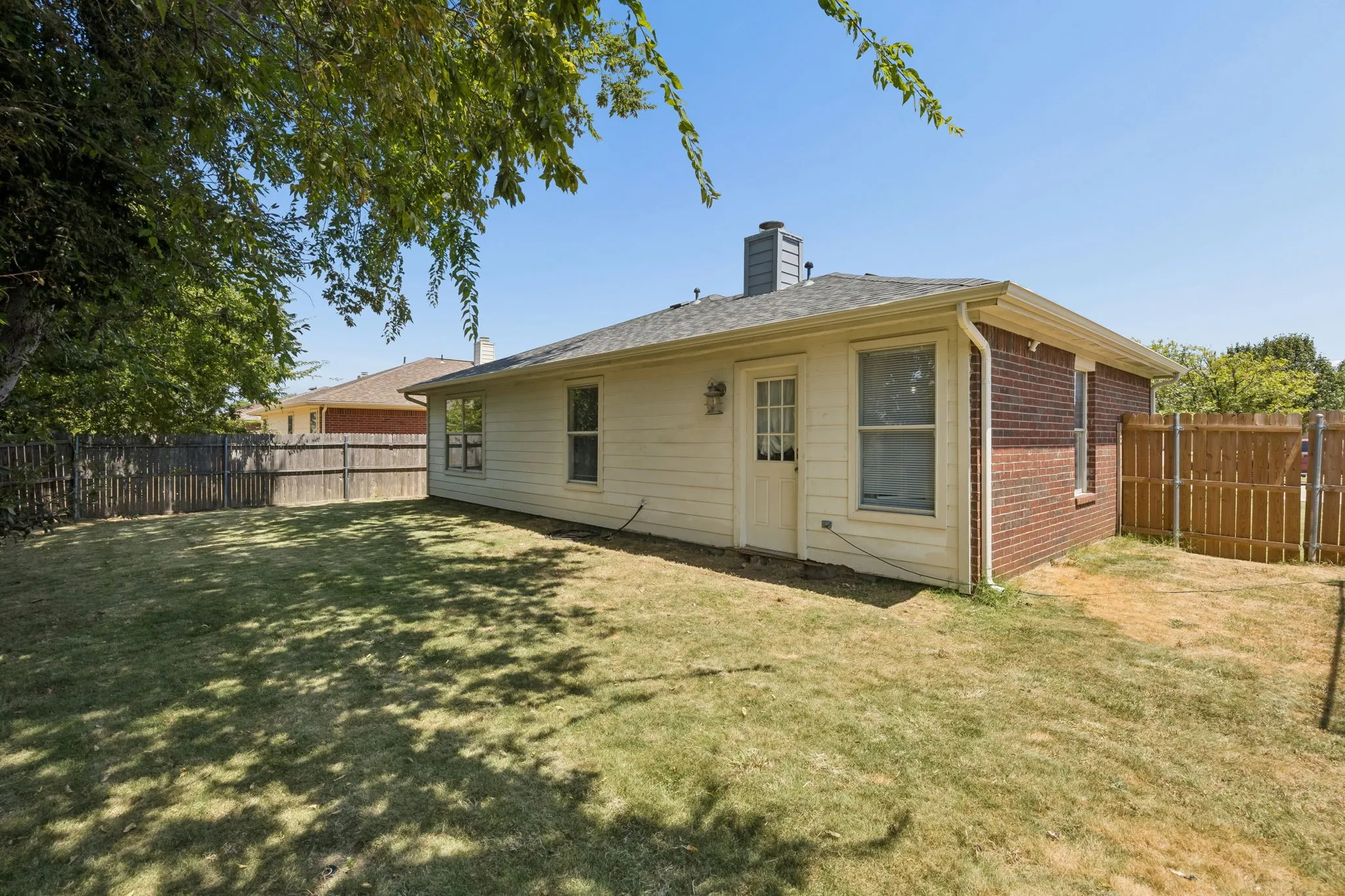 Expansive grassy area with wood fencing, brick and siding exterior, multiple windows, and a rear entry door