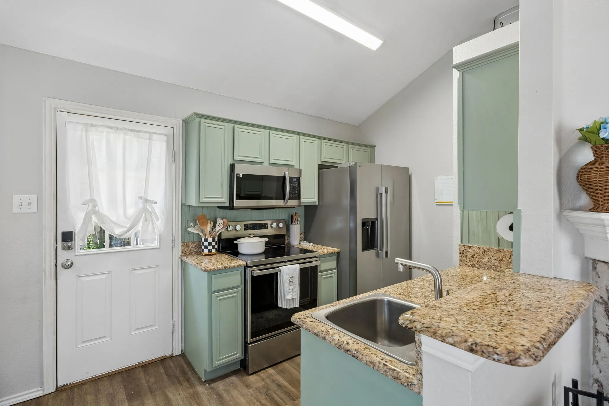 Kitchen featuring light green cabinetry, stainless steel appliances, speckled stone countertops, and wood-finish flooring