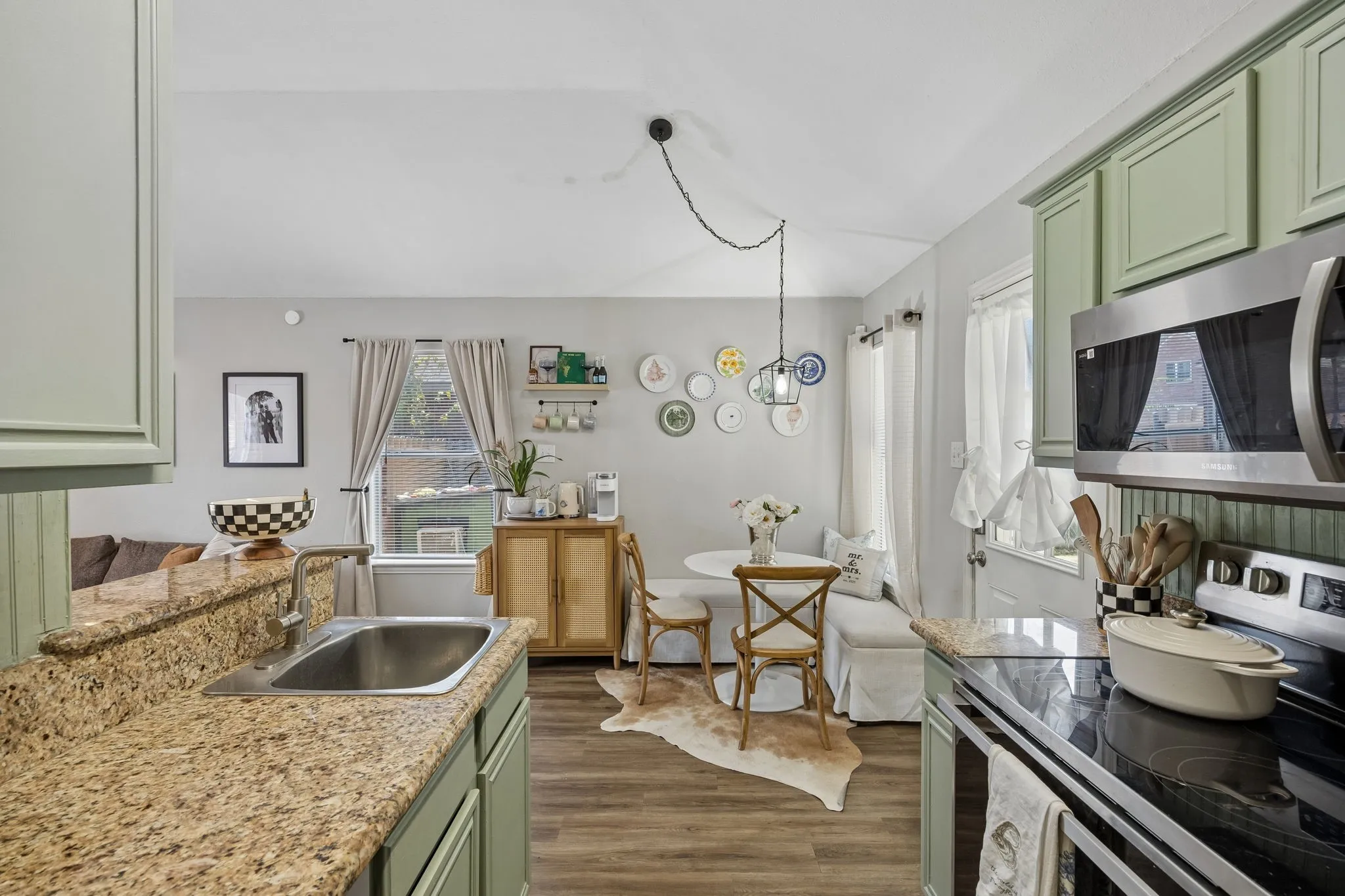 Kitchen featuring sage green cabinetry, stone-finish countertops, stainless steel microwave, and wood-finish flooring