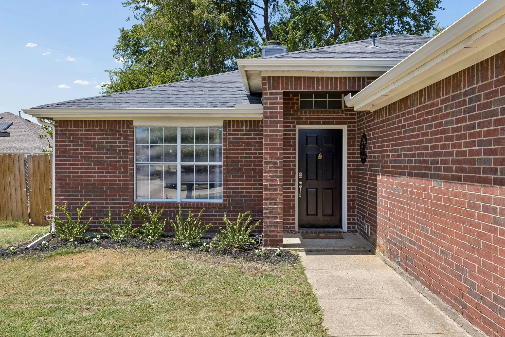Brick exterior with a dark panel door, white-framed window, and a concrete pathway